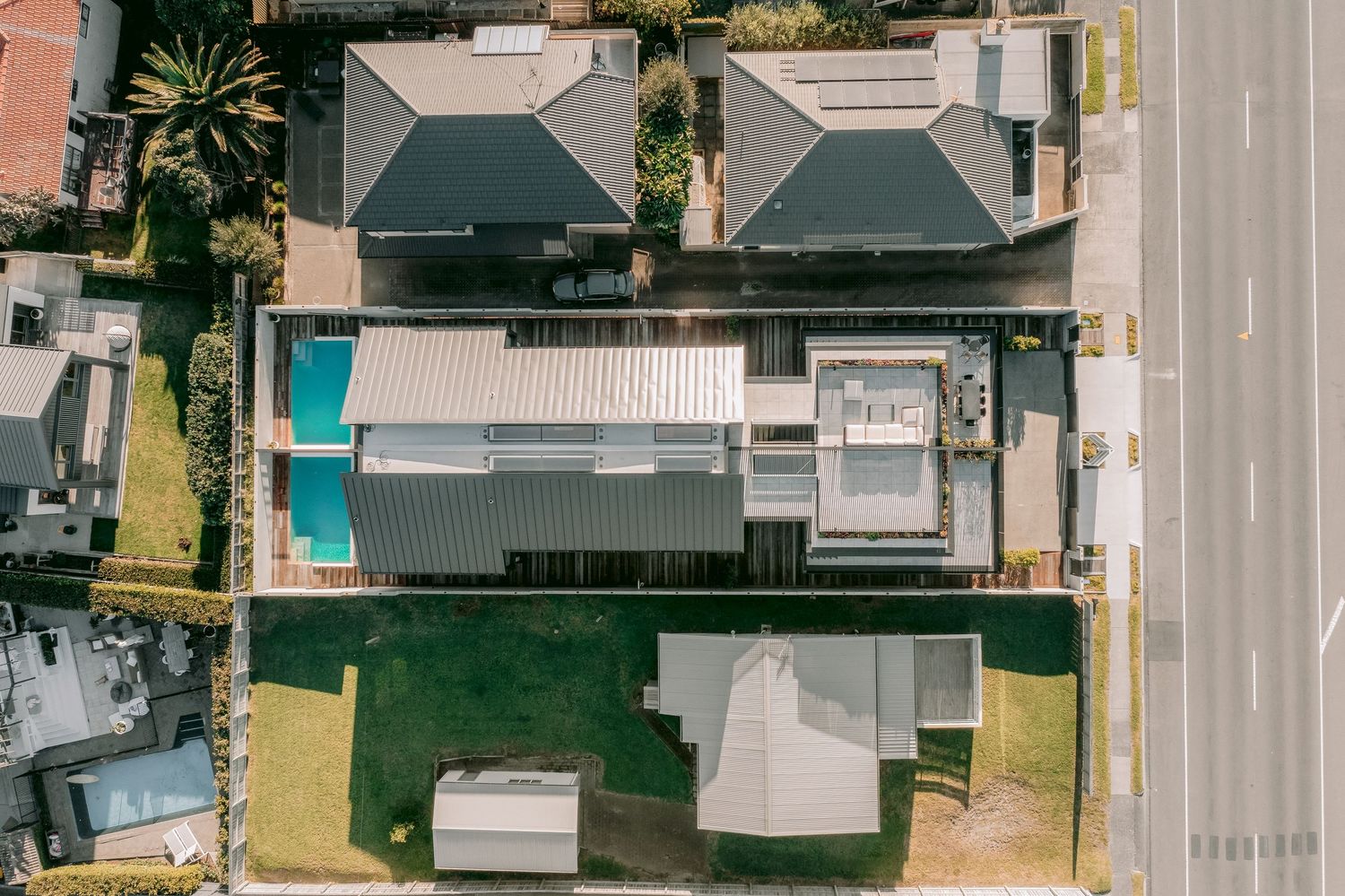 Aerial drone view of modern residential homes with solar panels and parked cars in suburban neighborhood.