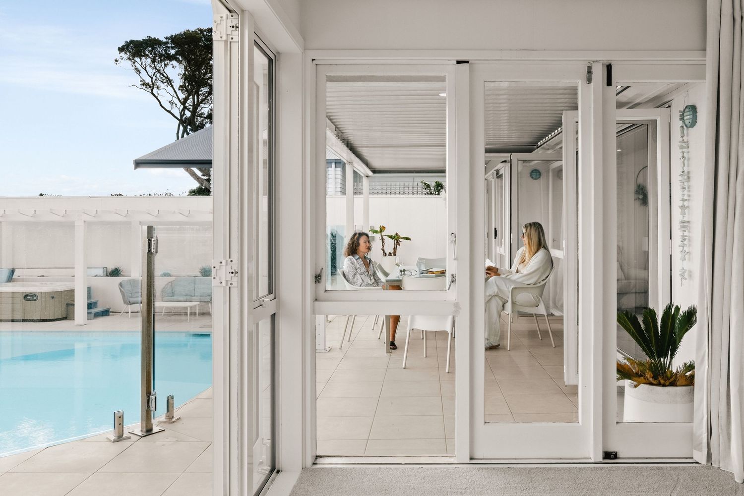 Modern glass-enclosed patio area overlooking swimming pool with outdoor furniture.