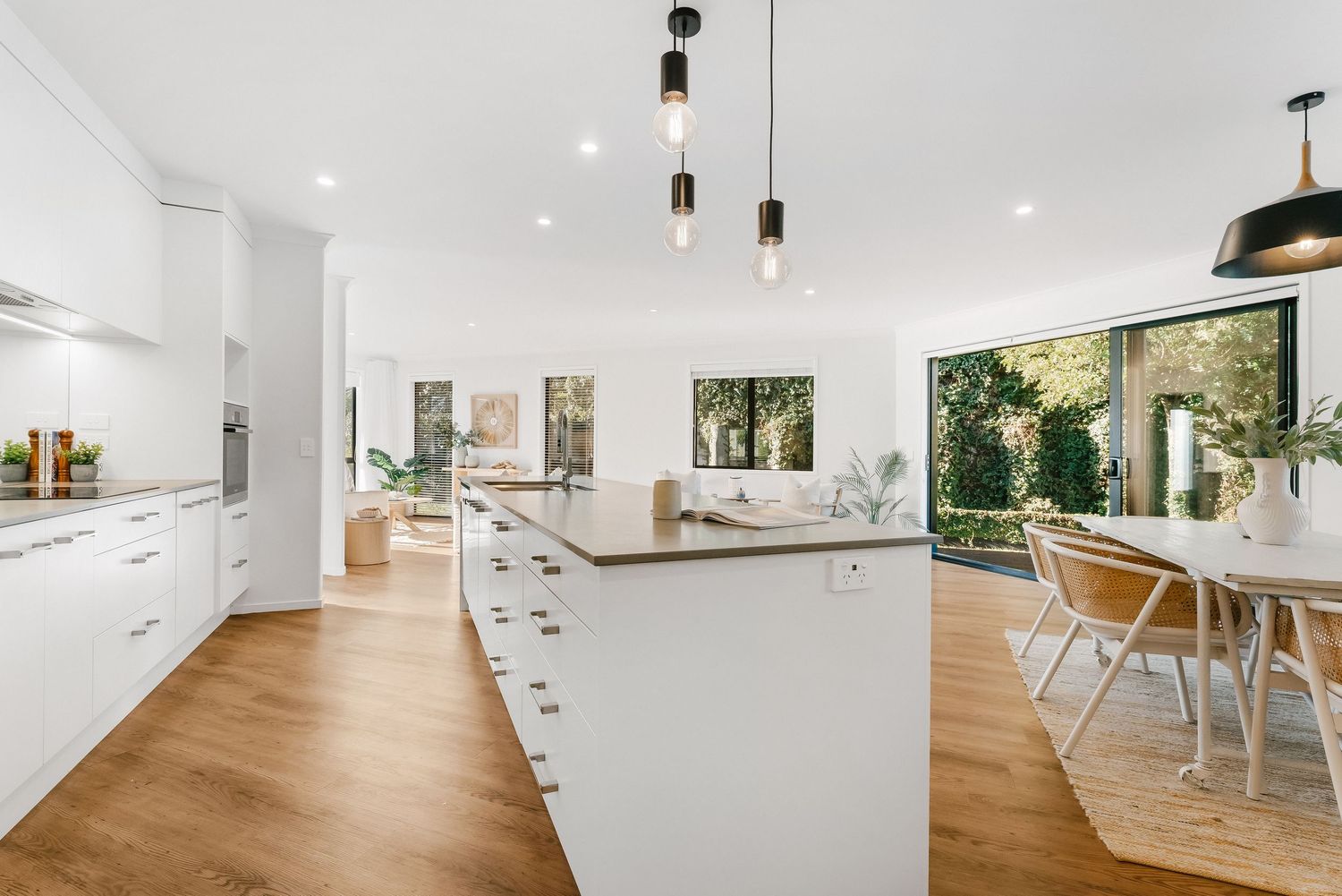 Modern open concept kitchen and dining area with white cabinets, hardwood floors and pendant lighting.