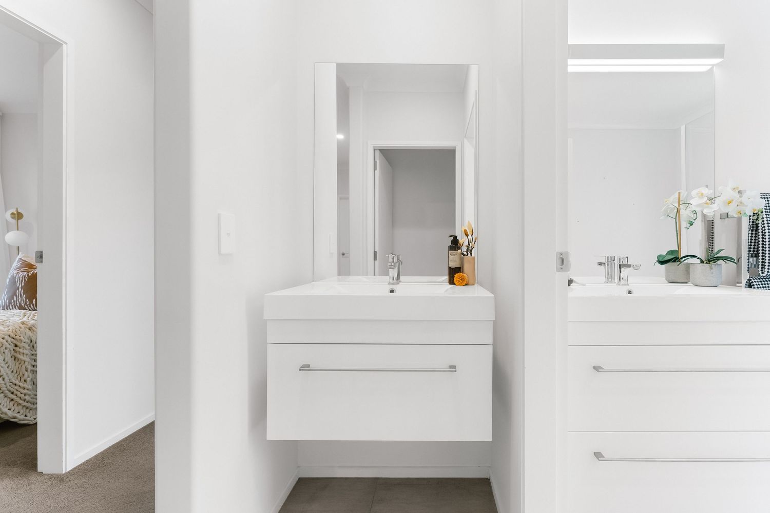 Modern white bathroom vanity with floating cabinets, large mirrors and sleek hardware in a minimalist design.