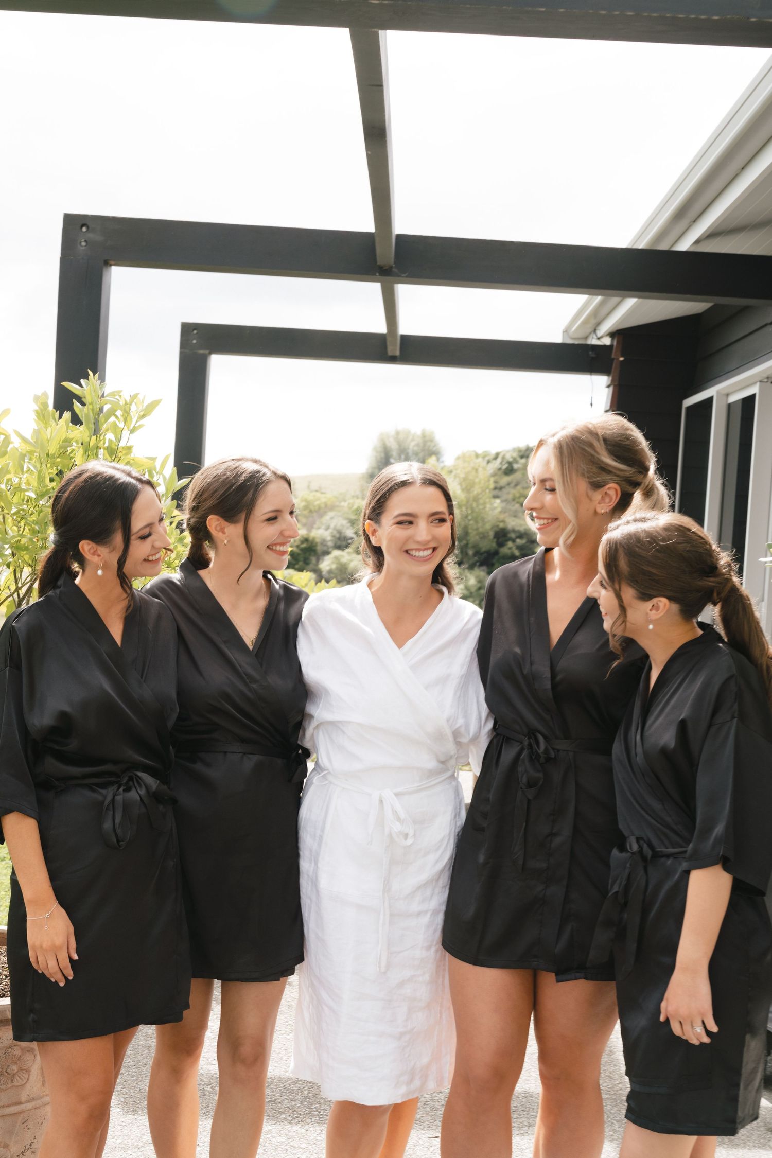 Wedding party members in black and white robes pose together outdoors.