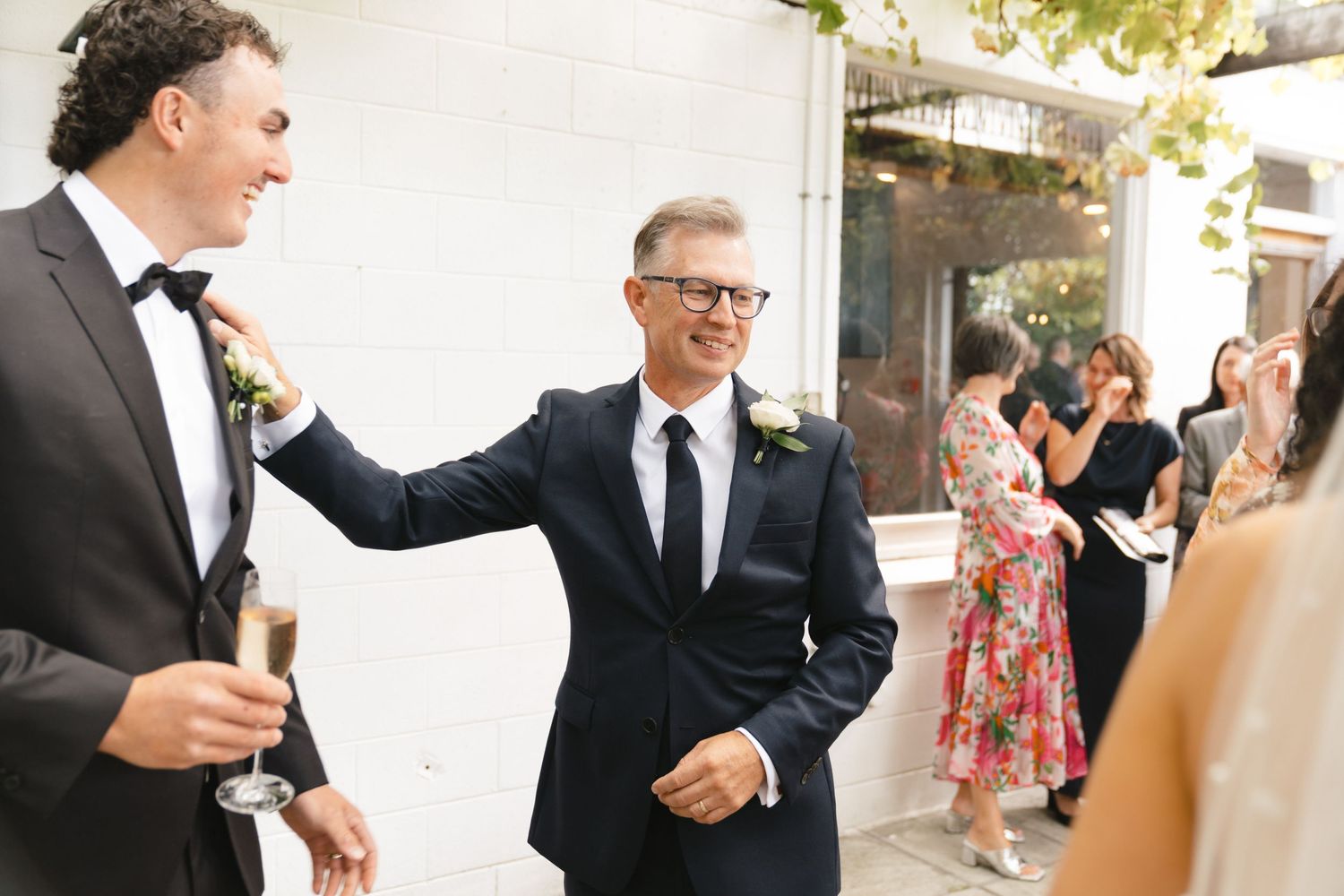 Two people in formal attire share a celebratory moment at an outdoor event while guests look on in the background.