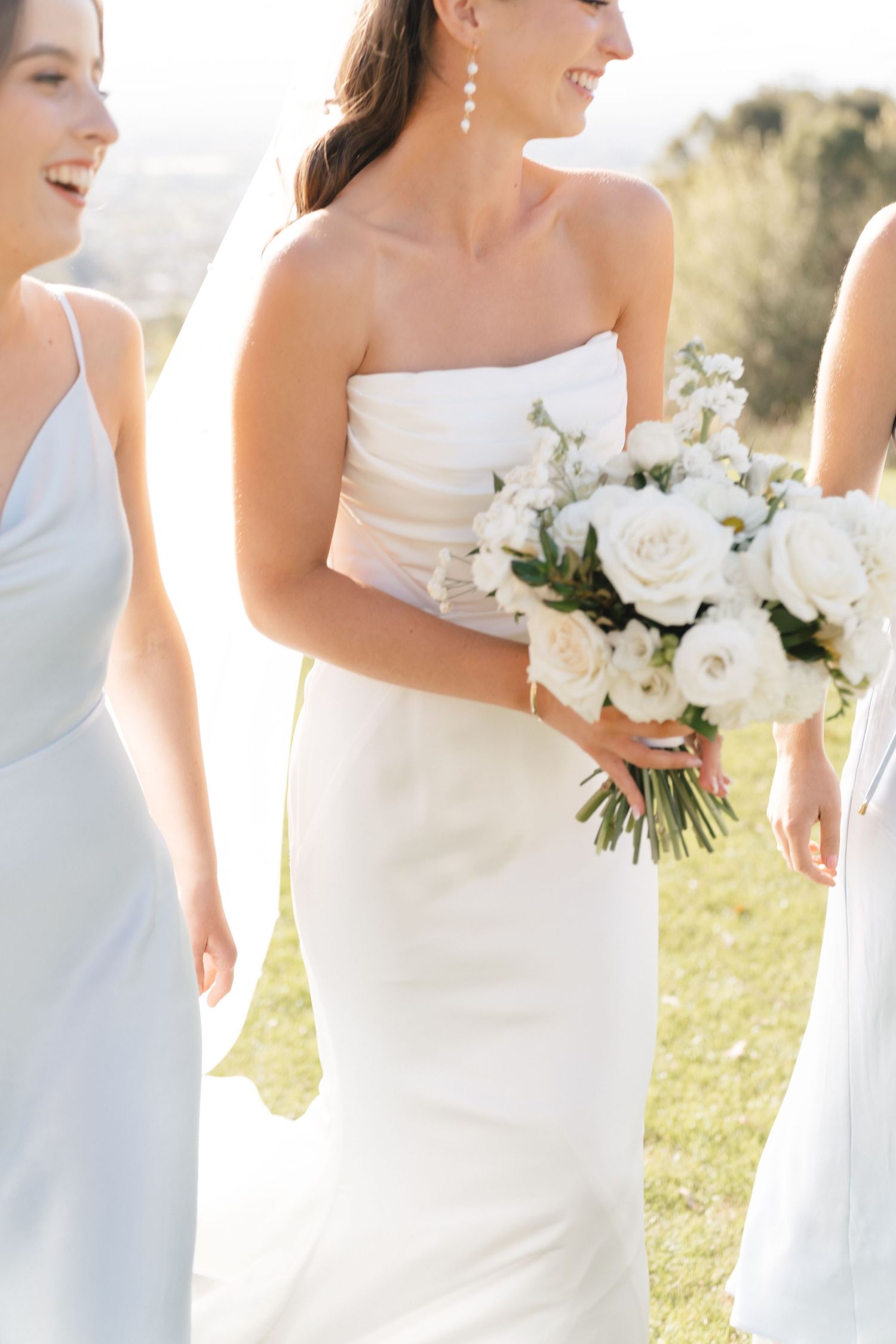 Wedding party in white and light blue dresses holding elegant white flower bouquets.