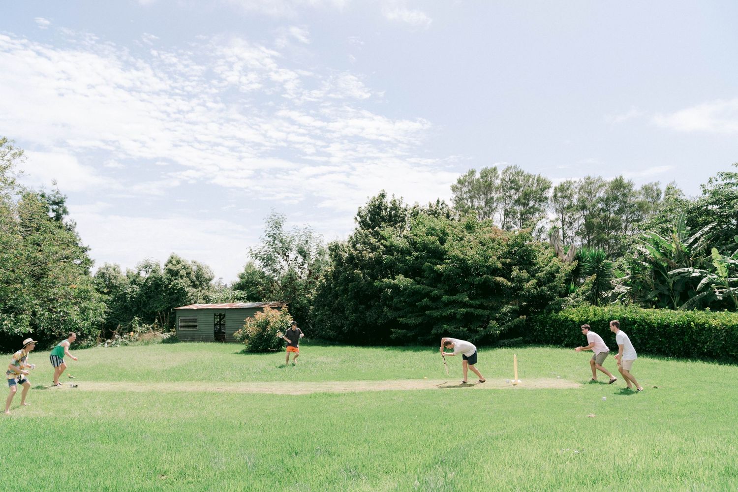 Group playing croquet on a lush green lawn surrounded by trees on a summer day.