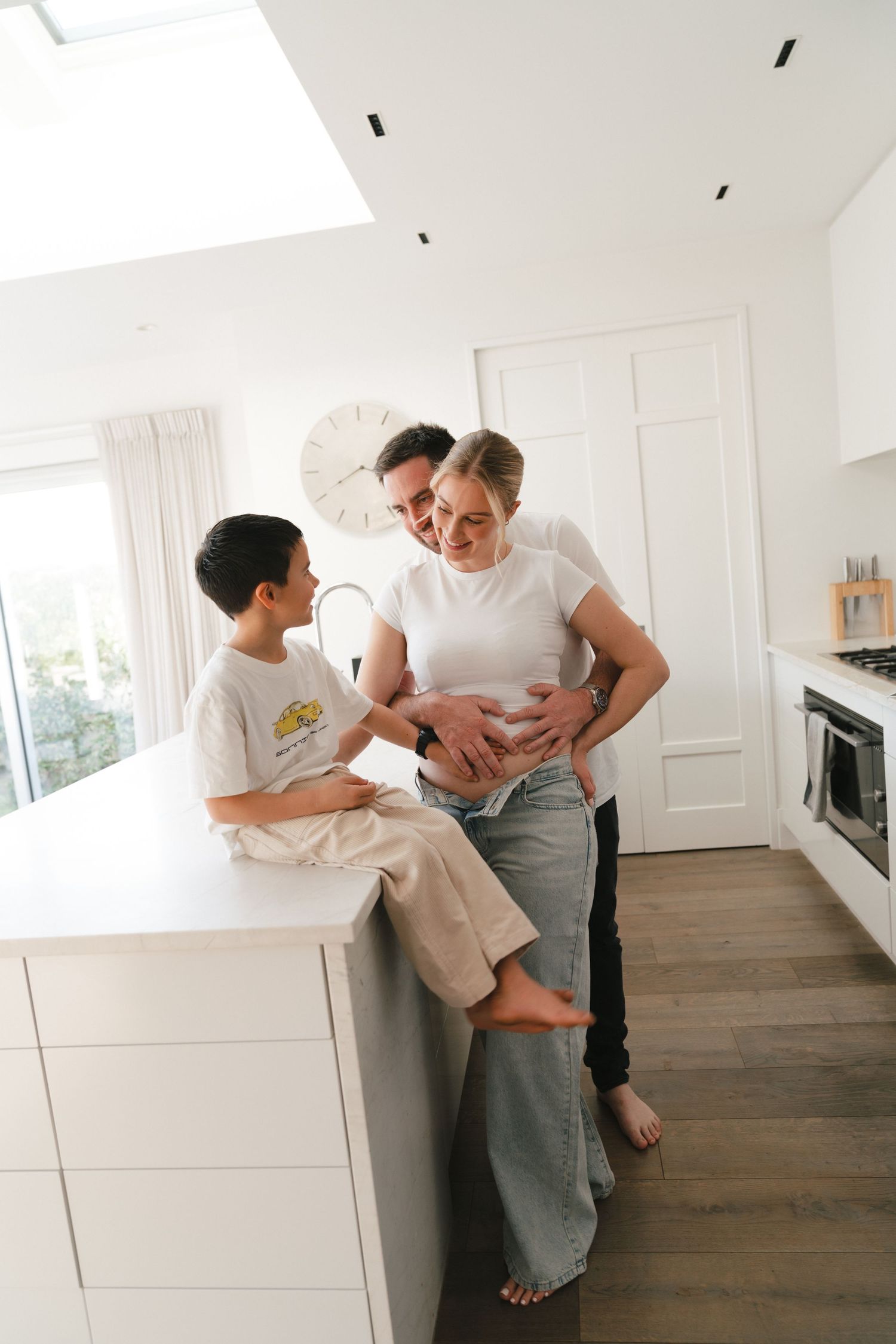 Family sharing an intimate moment together in a bright modern kitchen with white cabinetry and hardwood floors.