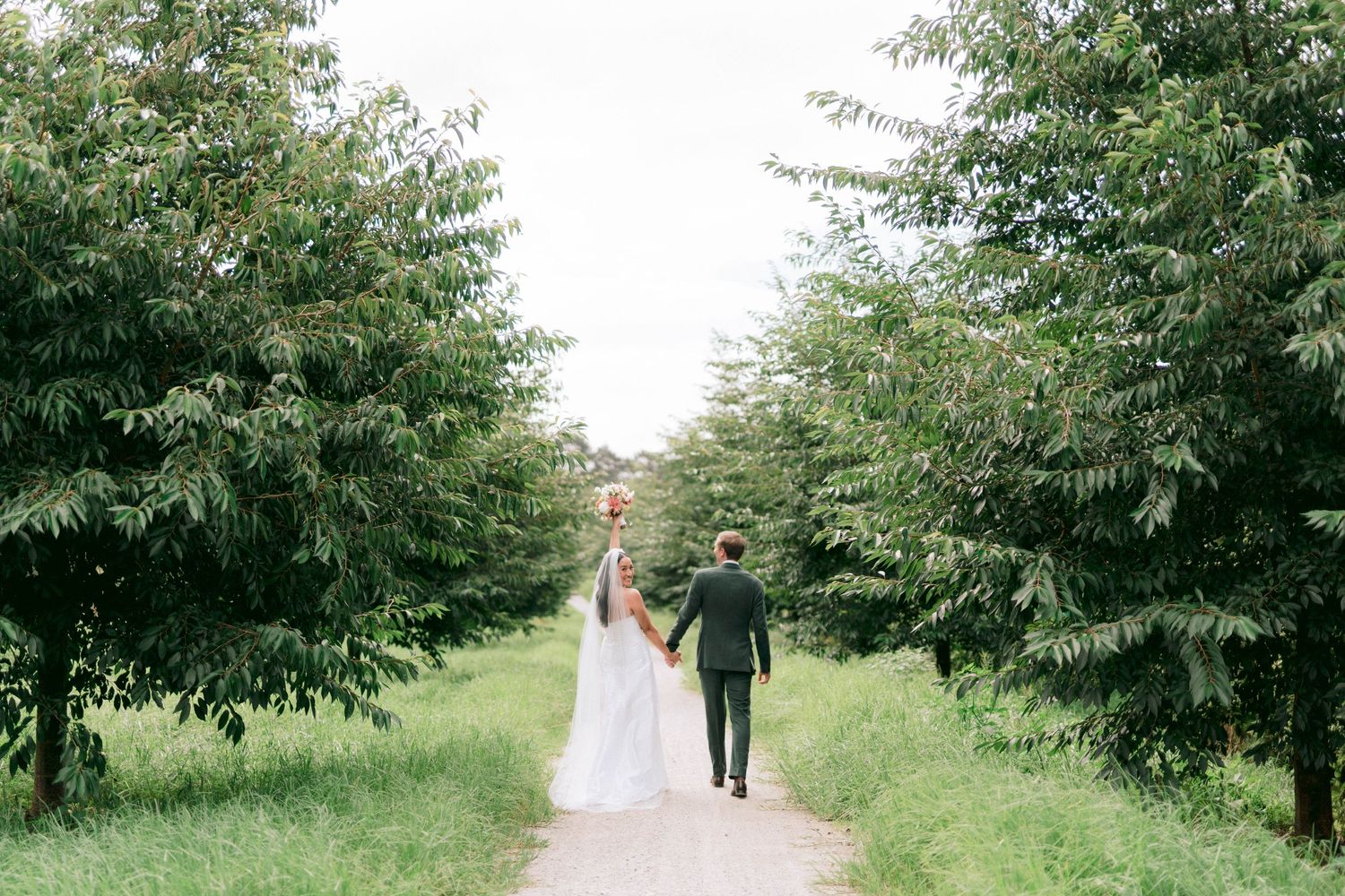 Couple walking down a tree-lined path during an outdoor wedding photoshoot.