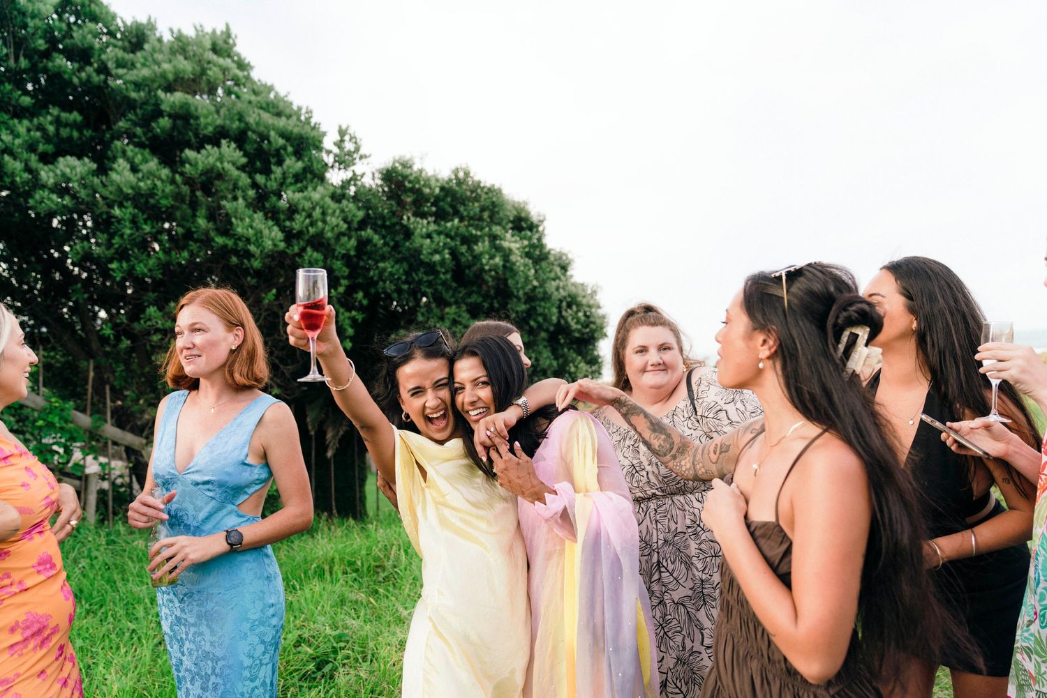 Friends in summer dresses laughing together in grassy outdoor setting.