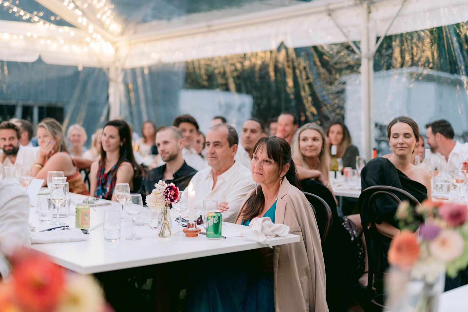 Wedding reception guests seated at decorated tables under a tent with twinkling lights.