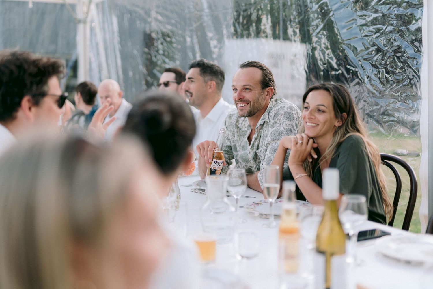 Wedding reception guests enjoying conversation and drinks under a clear tent.