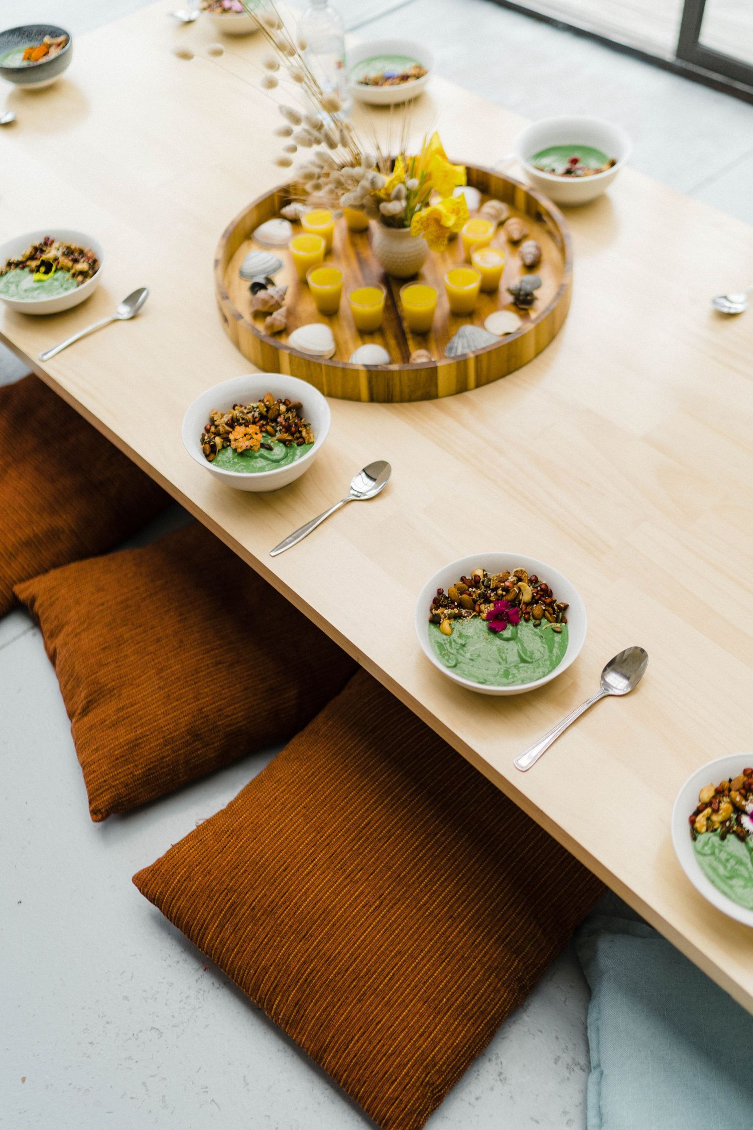 Colorful smoothie bowls and yellow drinks arranged on wooden serving tray with decorative flowers.