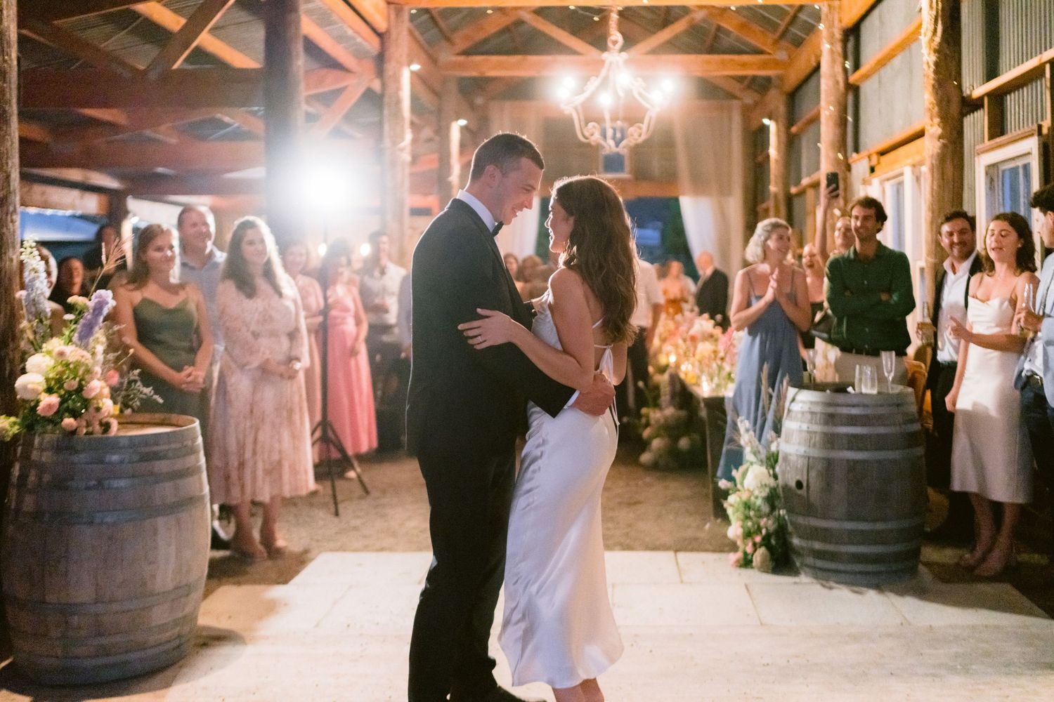 First dance moment in a rustic barn venue with wine barrels and ambient lighting.