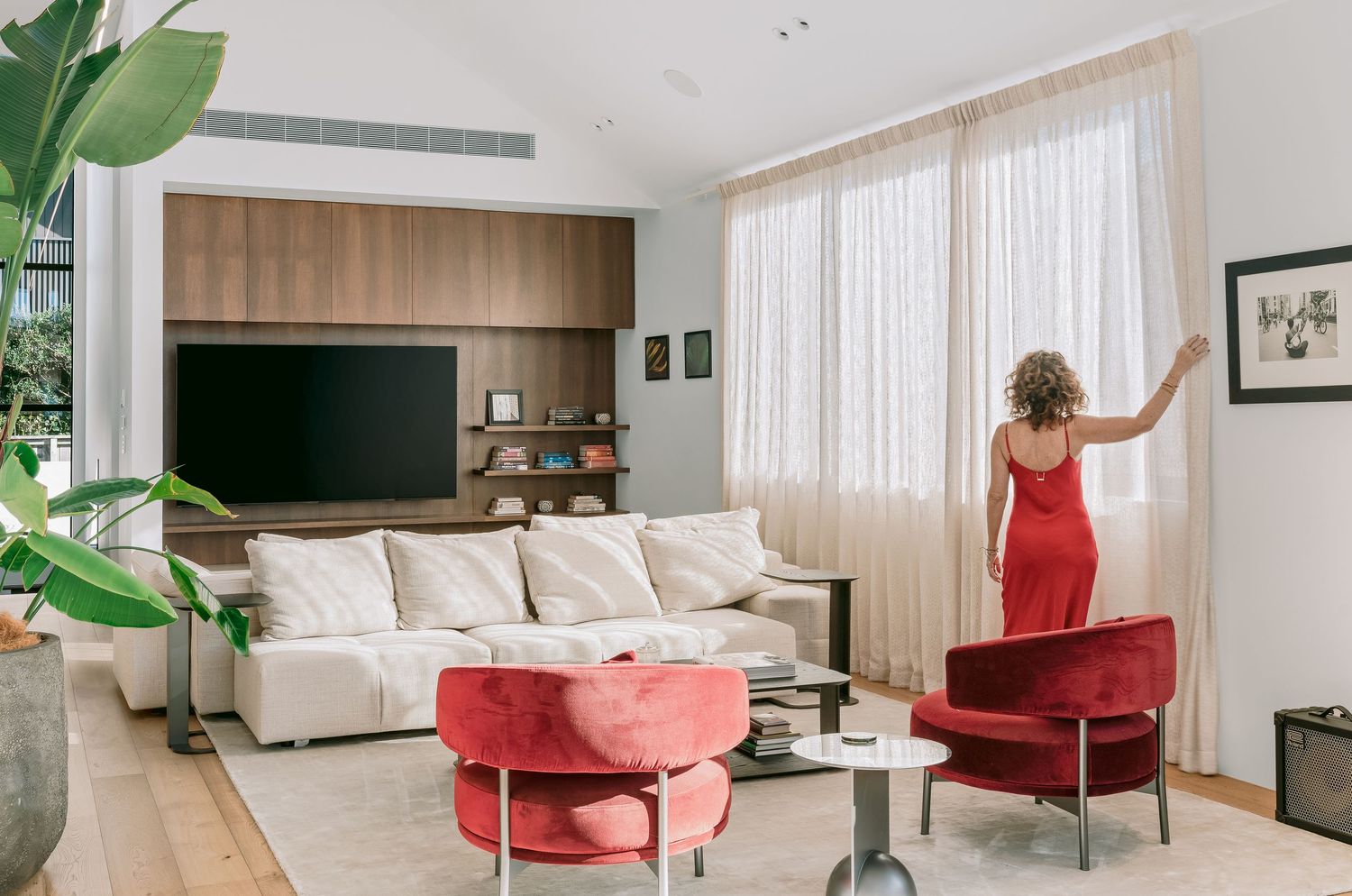 Stylish living room with built-in entertainment unit, red accent chairs, and large indoor plants.