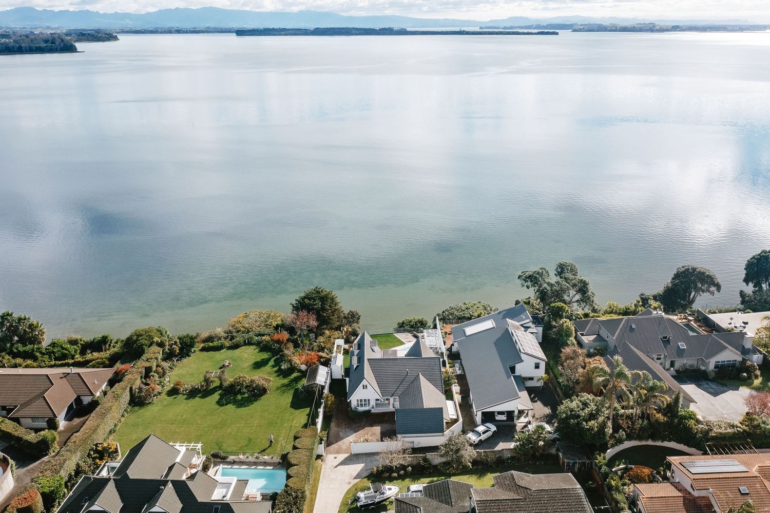 Aerial view of waterfront homes along a calm bay with mountains in the distance.