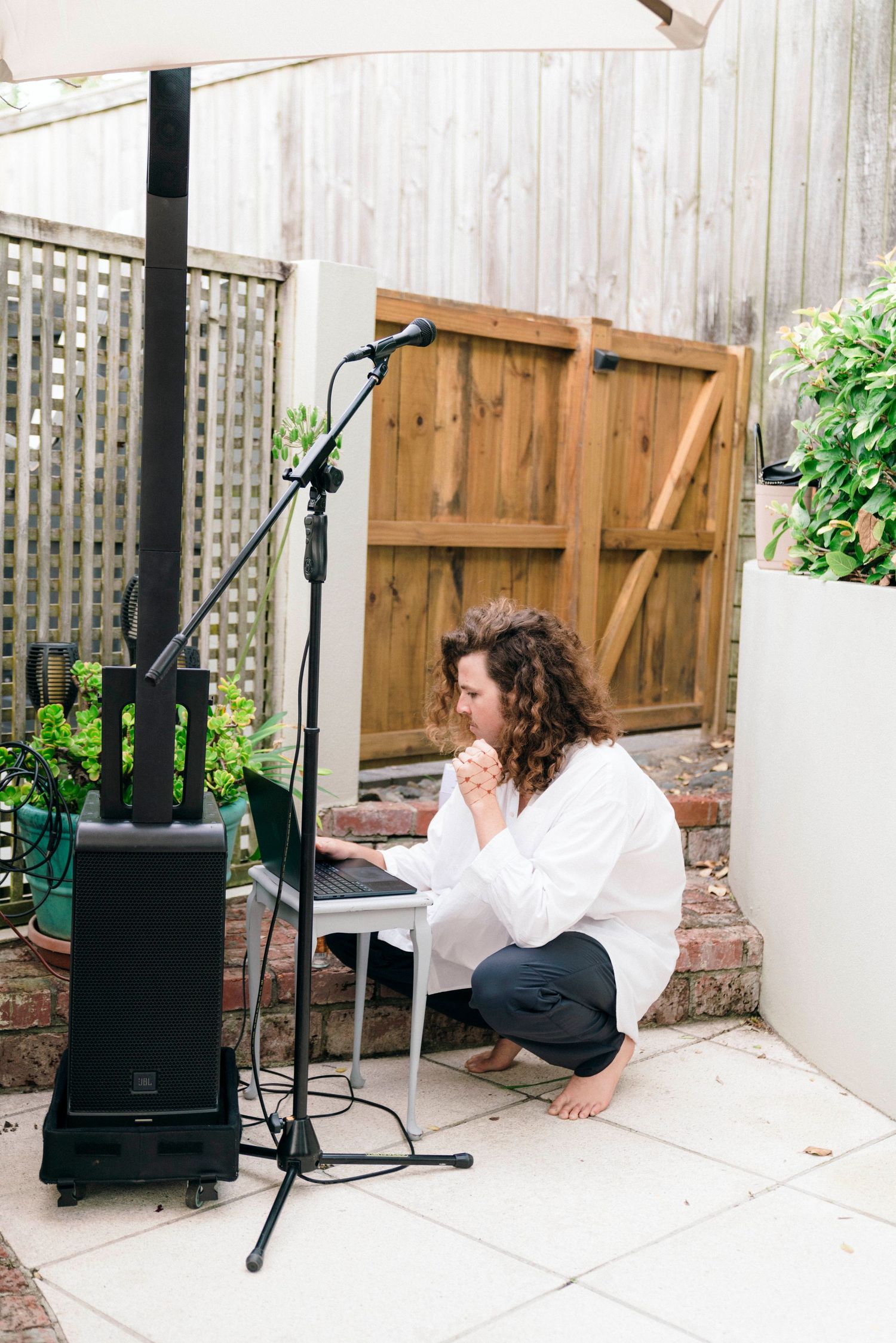 Person in white clothing reclining on outdoor patio next to wooden fence and planters.