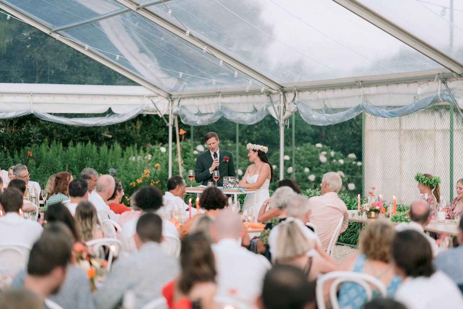 Wedding guests watching speakers at an outdoor tented reception.