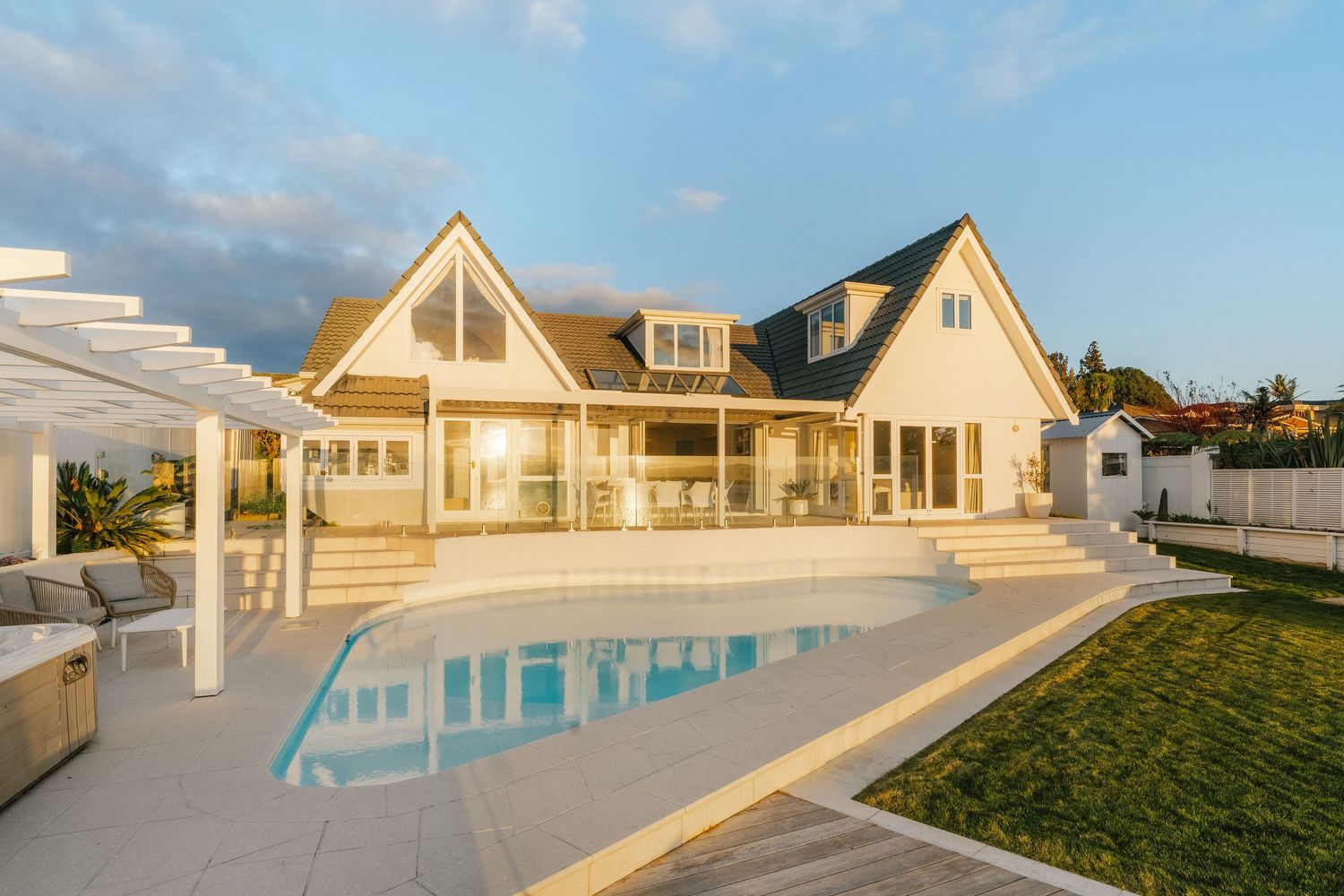 Luxurious white coastal home with swimming pool and pergola at sunset.