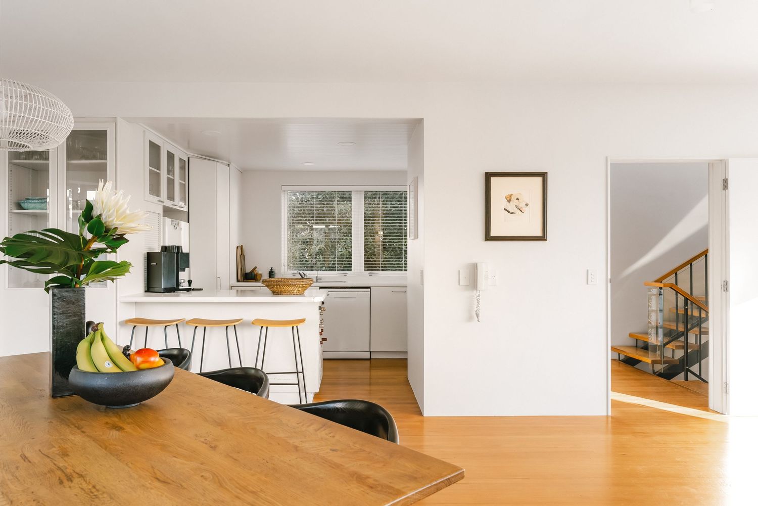 Open plan kitchen and dining area with wooden table, black chairs and white cabinets.