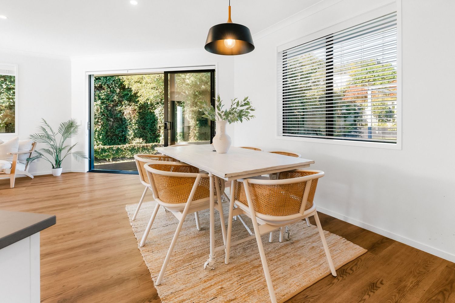 Bright dining area featuring wooden floors, white walls and multiple windows overlooking natural greenery.