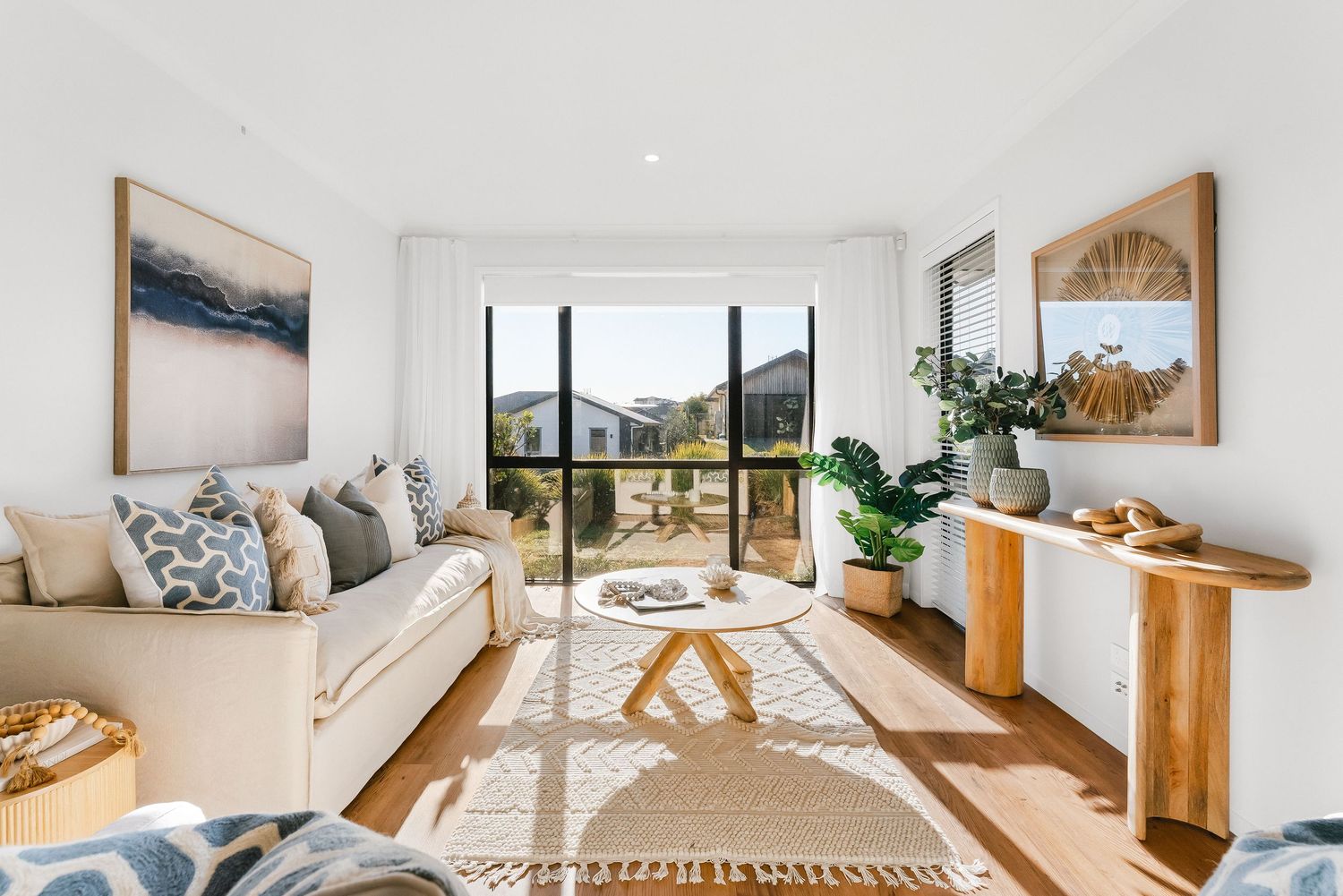 Contemporary sunlit living area featuring a neutral sofa, wooden console table and scenic mountain views through large windows.