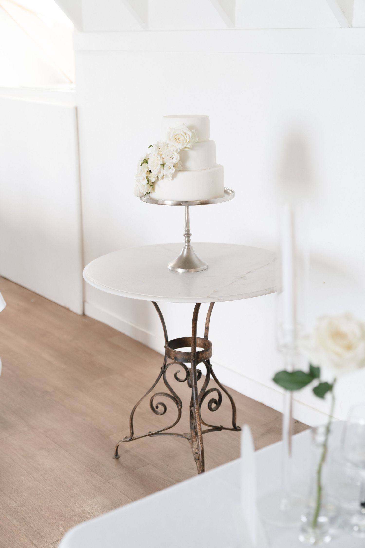 Elegant white wedding cake with floral decoration displayed on vintage metal table.