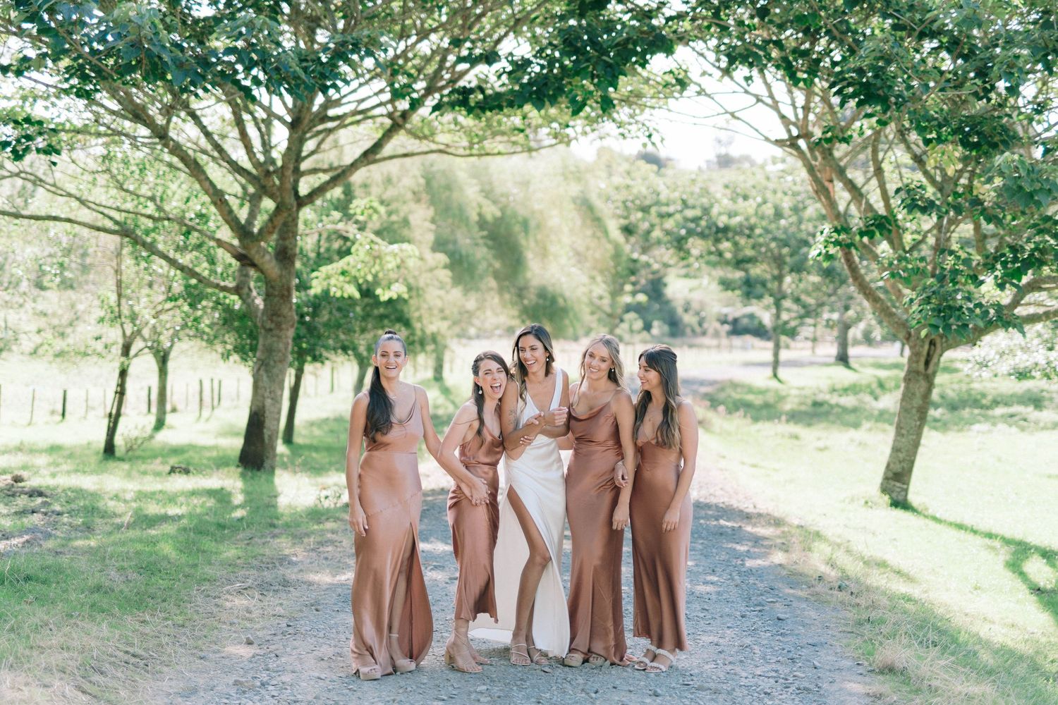 Wedding party members pose for group photos on a tree-lined path in coordinated attire.