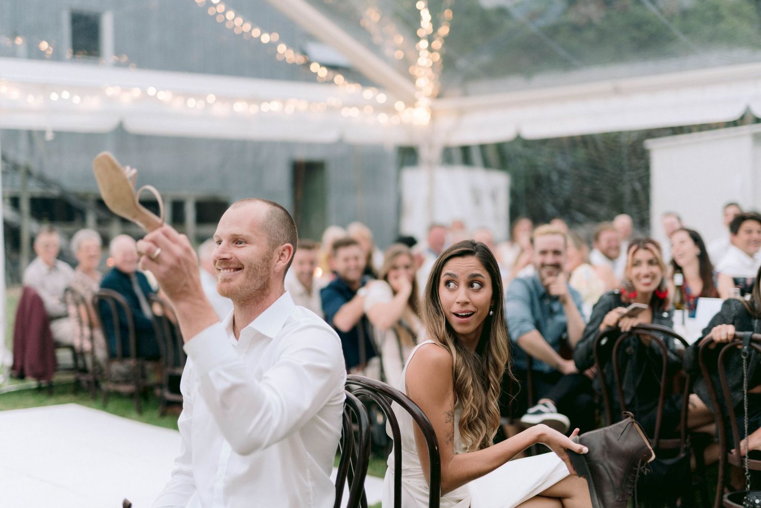 Wedding celebration under a clear tent with string lights creating a magical atmosphere.