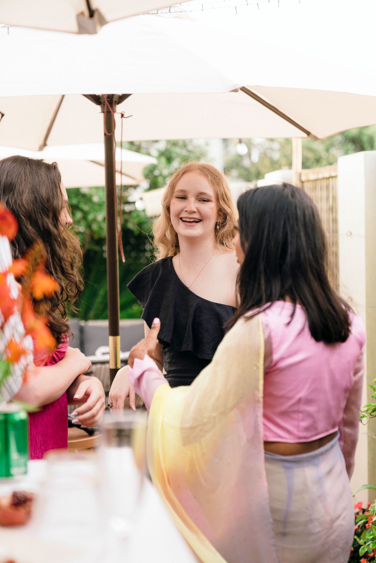 Group of people mingling under patio umbrella at outdoor social gathering.