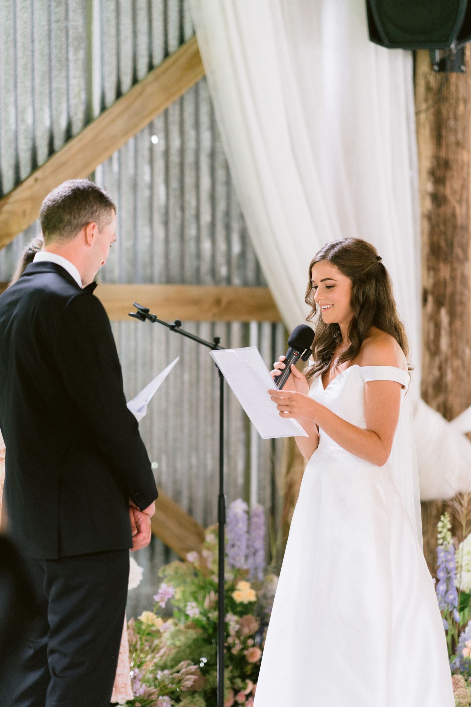 A couple exchanges vows during an intimate ceremony in a rustic barn setting with white drapes.