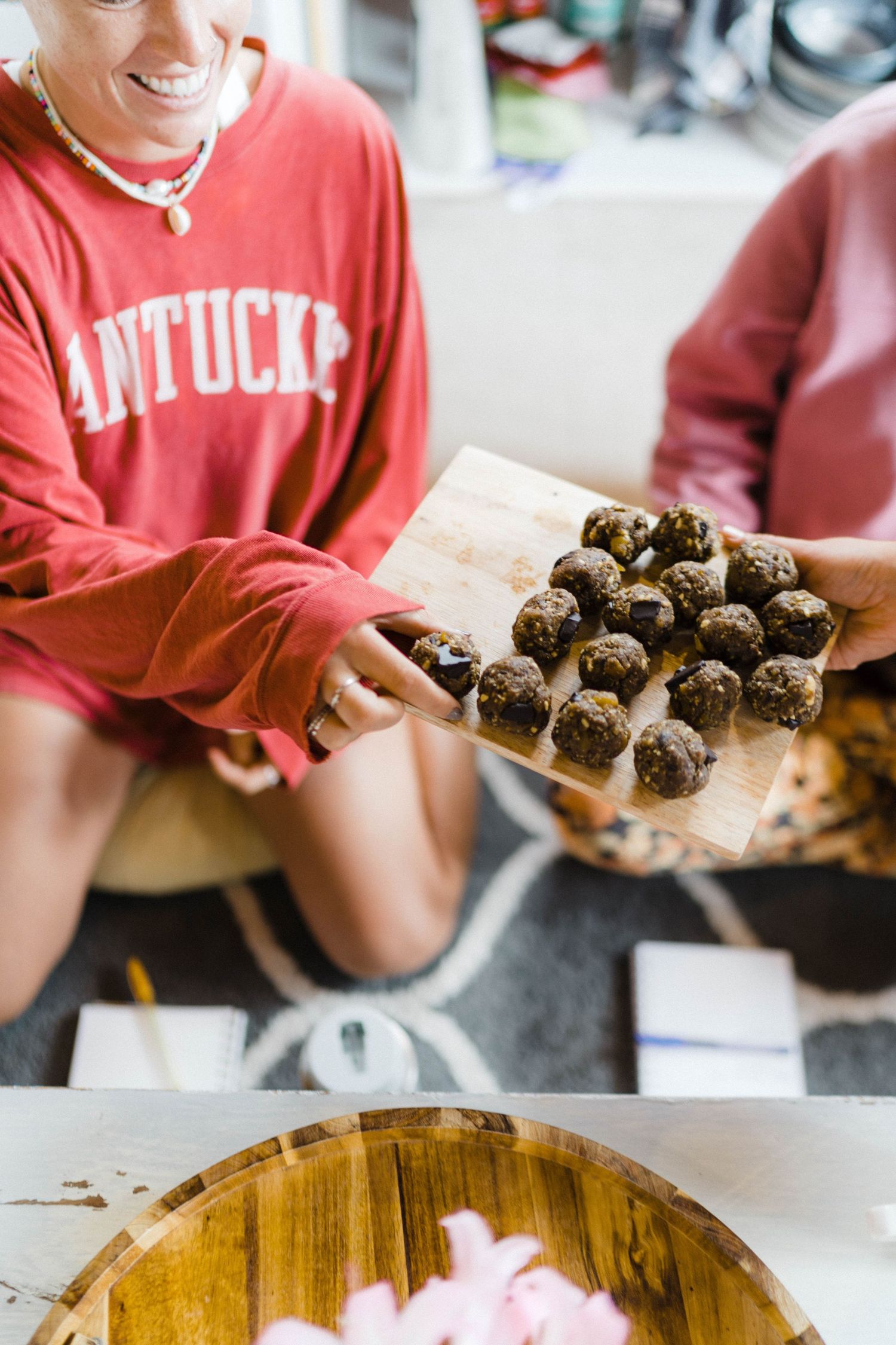 A person holds a wooden board displaying homemade chocolate energy balls.