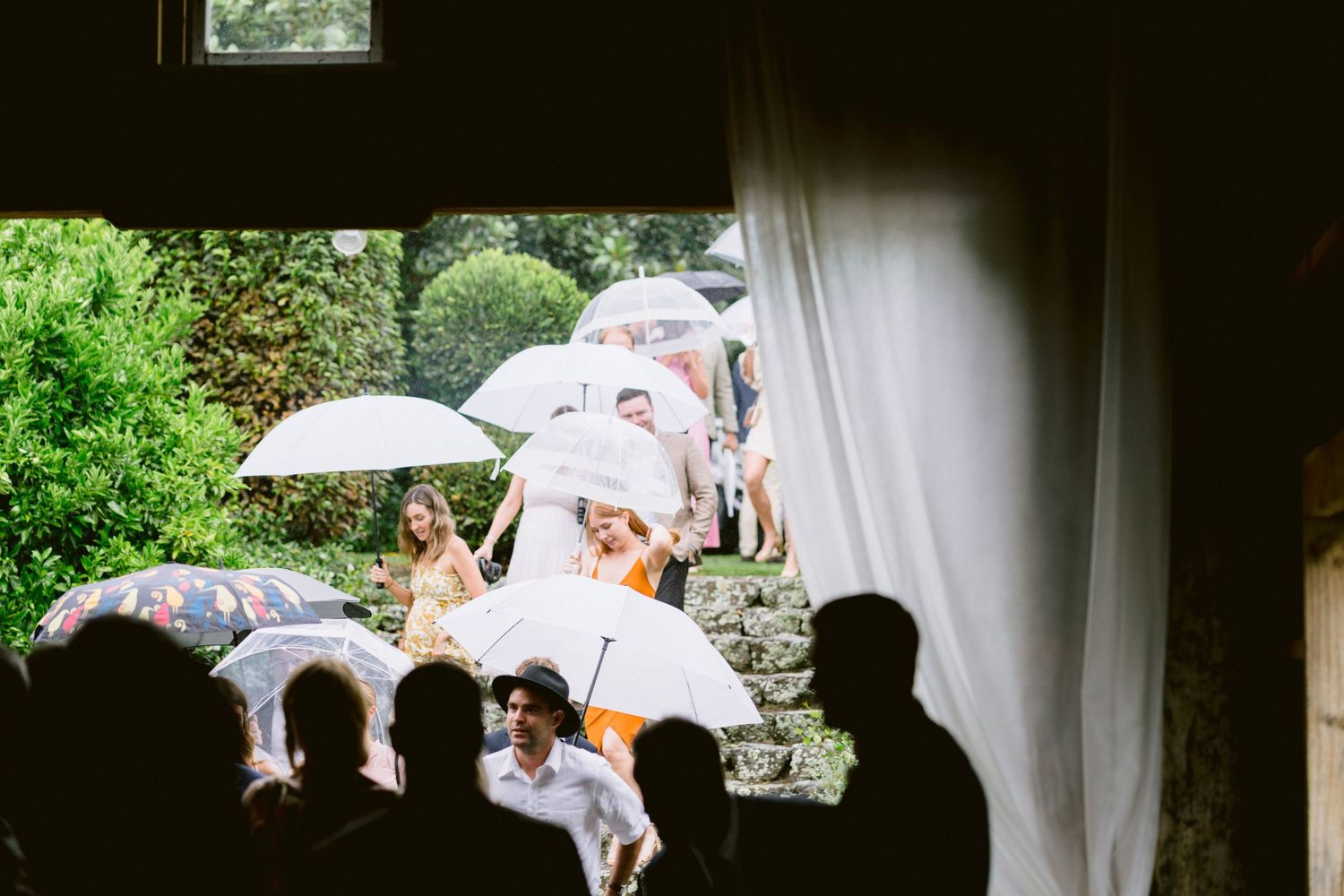 Group gathering under parasols on garden steps during a rainy outdoor event.