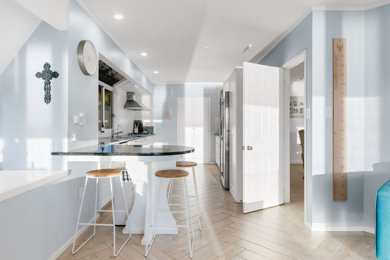 Modern white kitchen with bar stools and light blue walls features clean lines and minimalist design elements.