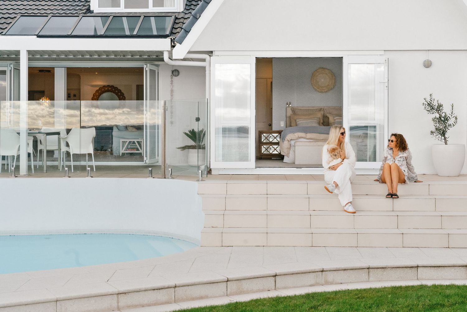 White tiled outdoor pool area with contemporary landscaping and glass barriers.