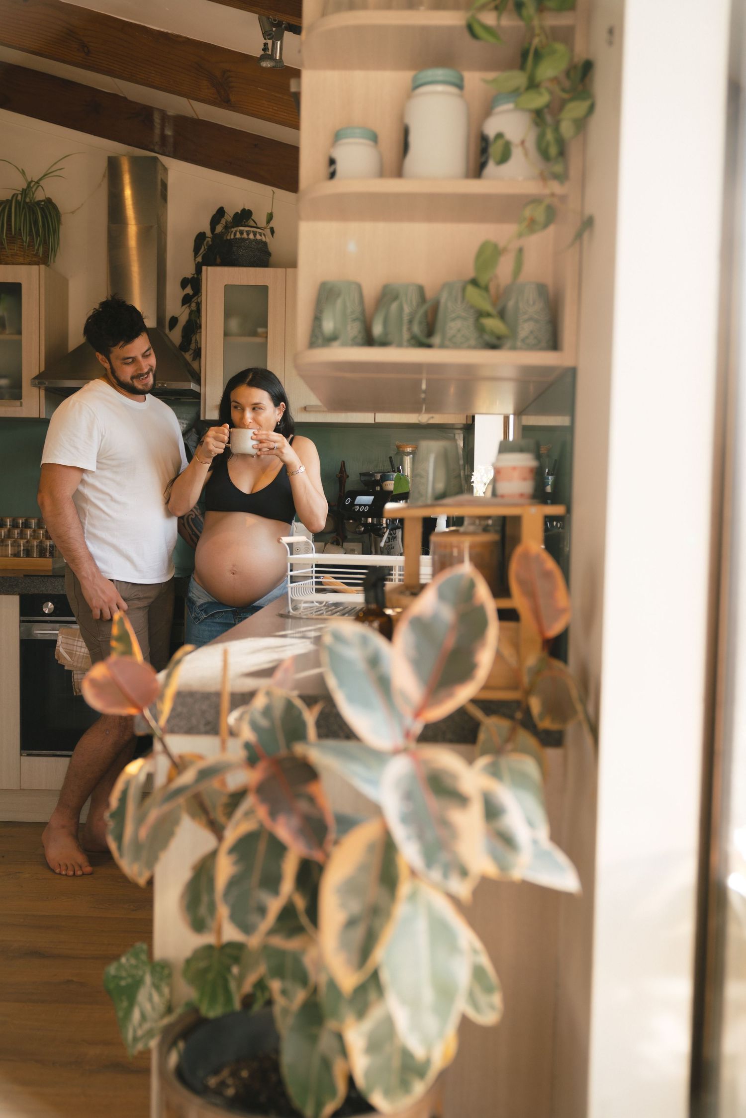 A cozy kitchen scene with decorative shelves, houseplants, and a couple enjoying morning coffee together.