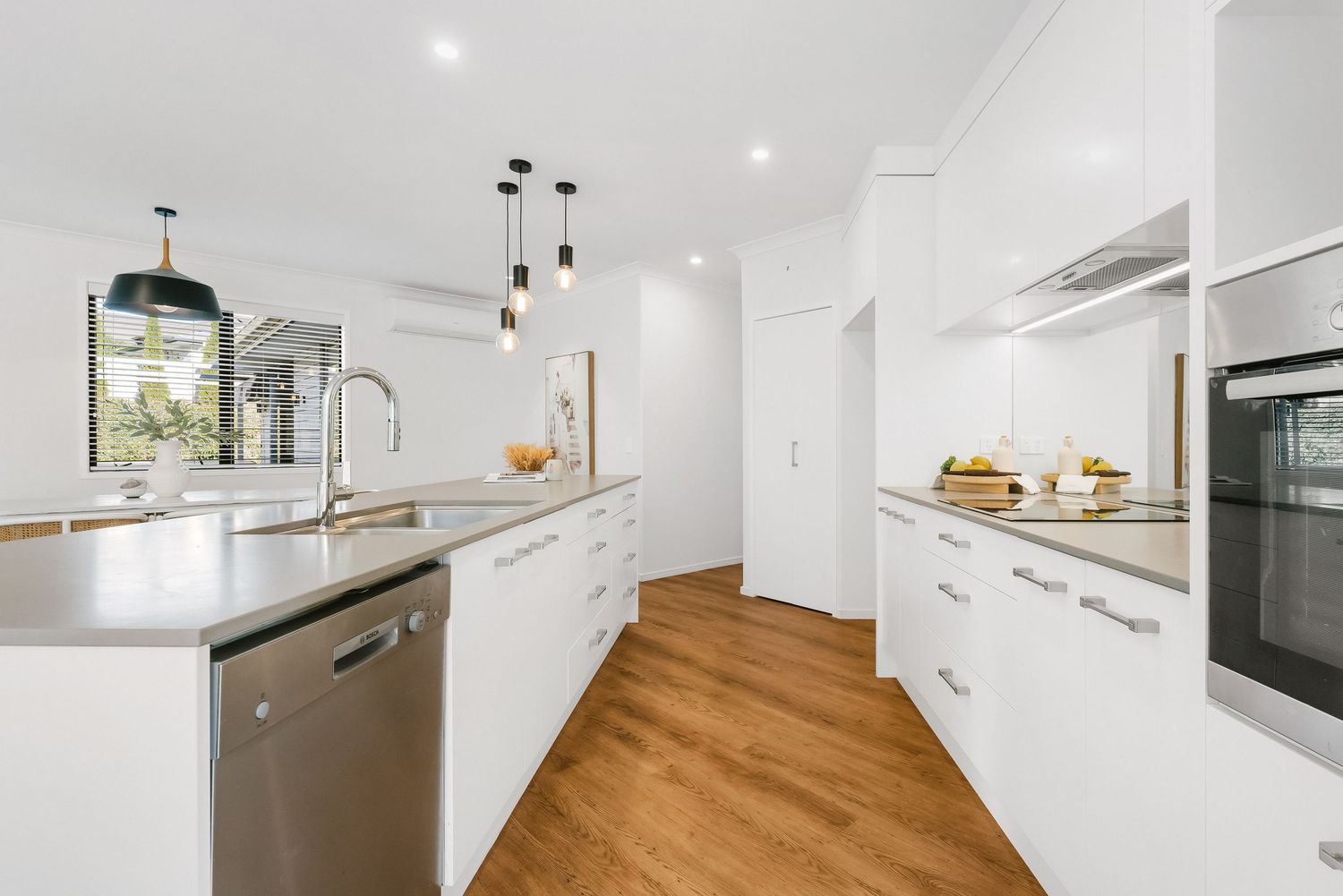 Contemporary white kitchen featuring sleek cabinetry, wooden flooring, and stainless steel appliances.