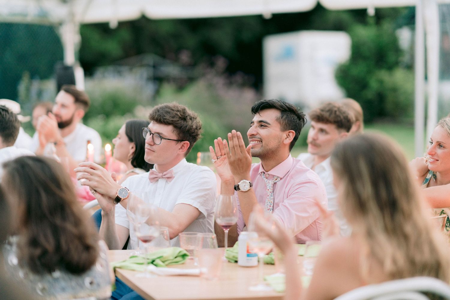 Wedding guests celebrate at an outdoor reception under a tent on a summer day.