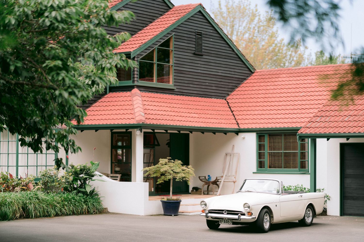 Classic white vintage car parked in front of a house with red roof tiles.