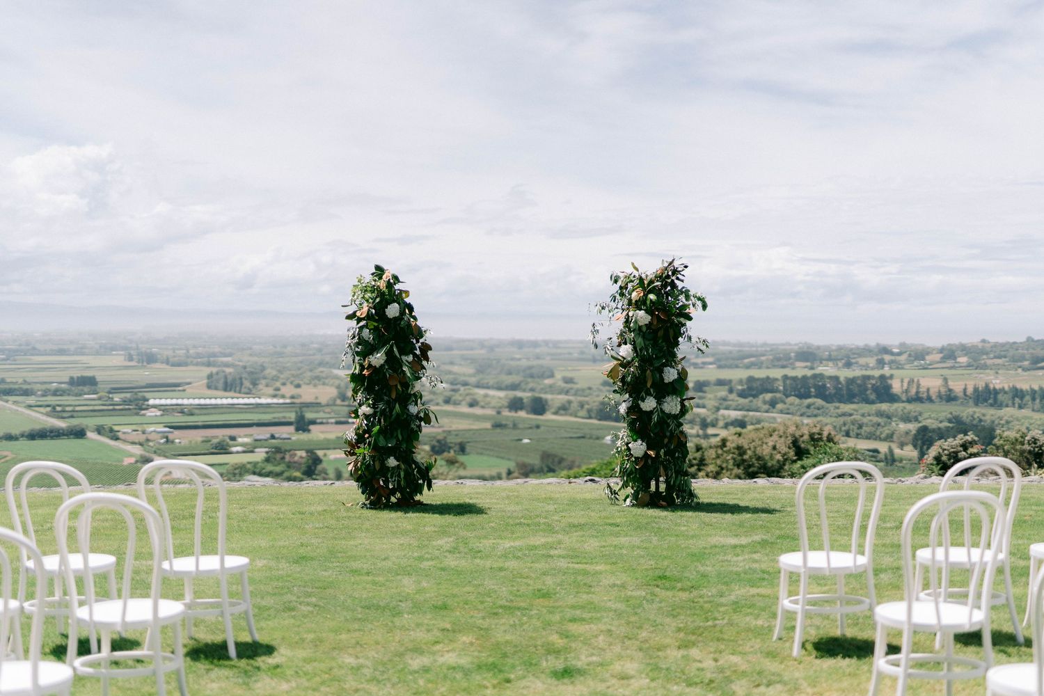 Outdoor wedding setup with white chairs arranged on a hilltop overlooking countryside.