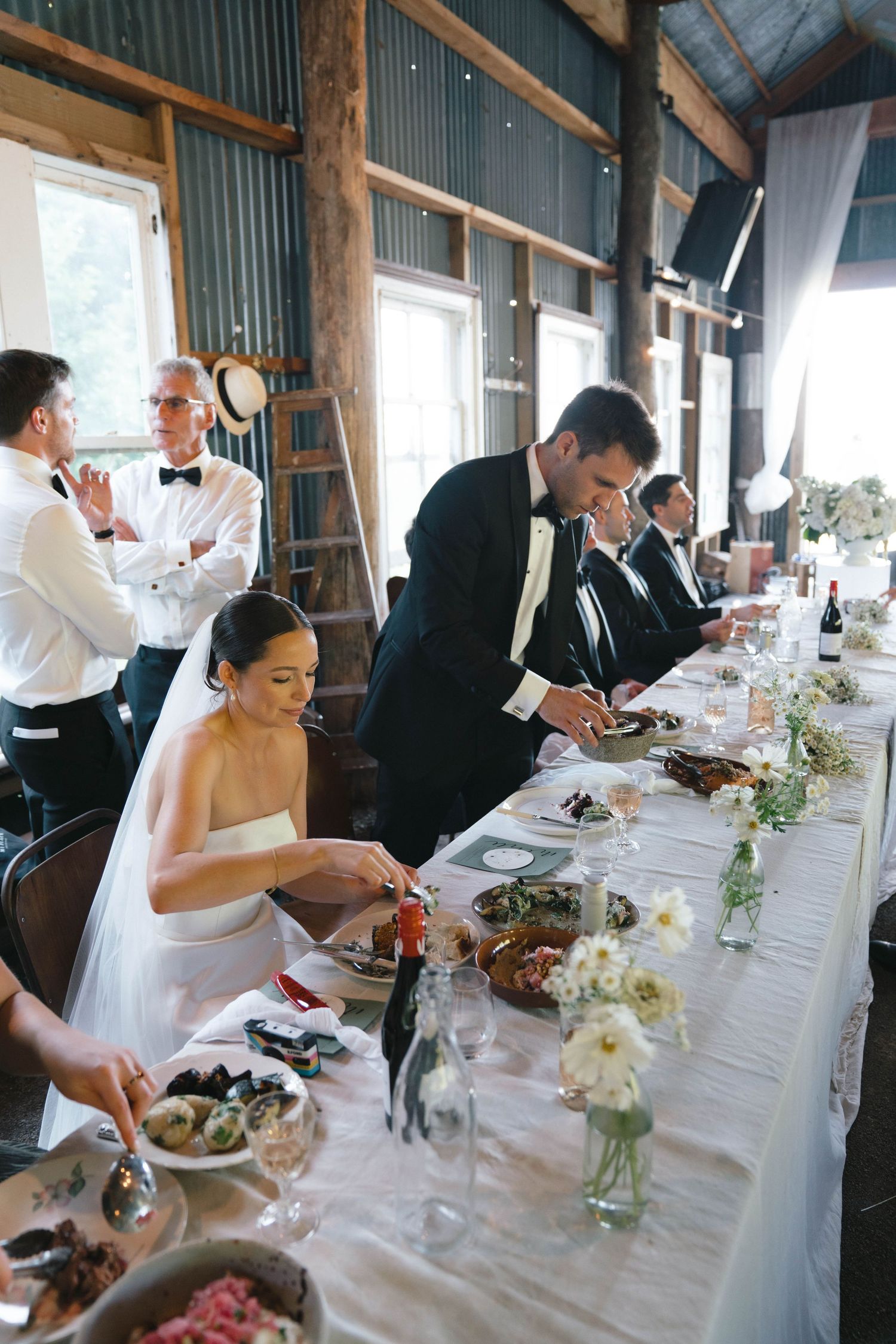 Wedding reception in rustic barn venue with elegant table settings and floral centerpieces.