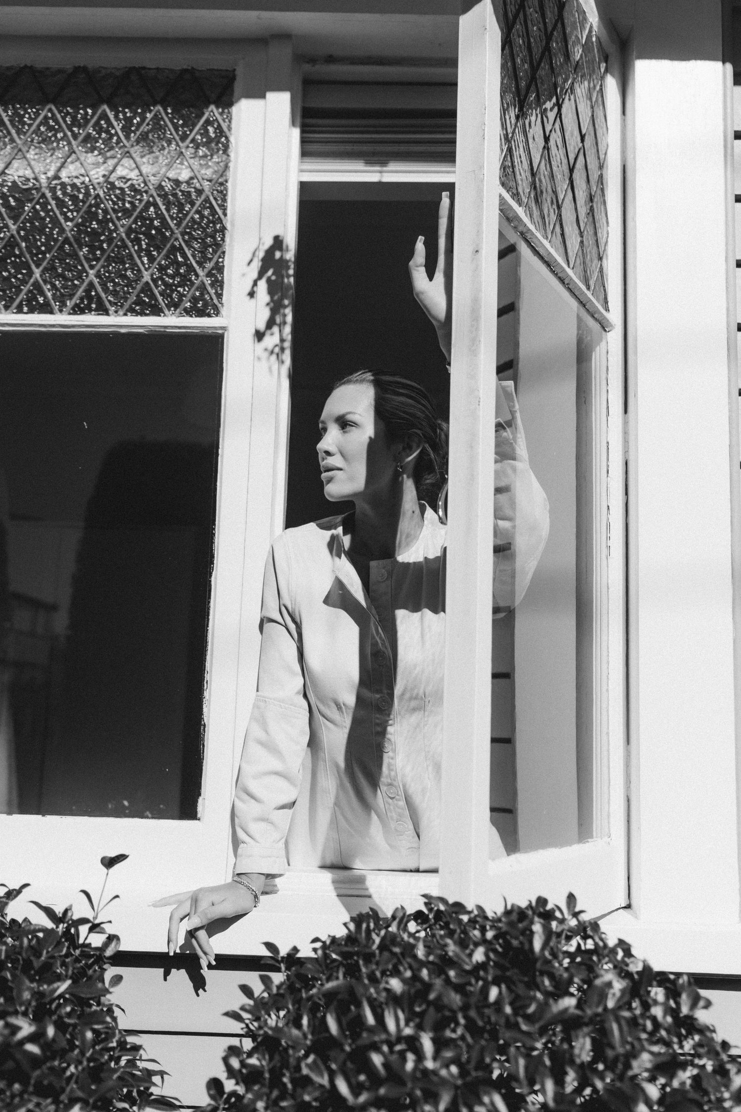 A silhouette appears between white-framed windows with diamond patterns above green shrubbery.