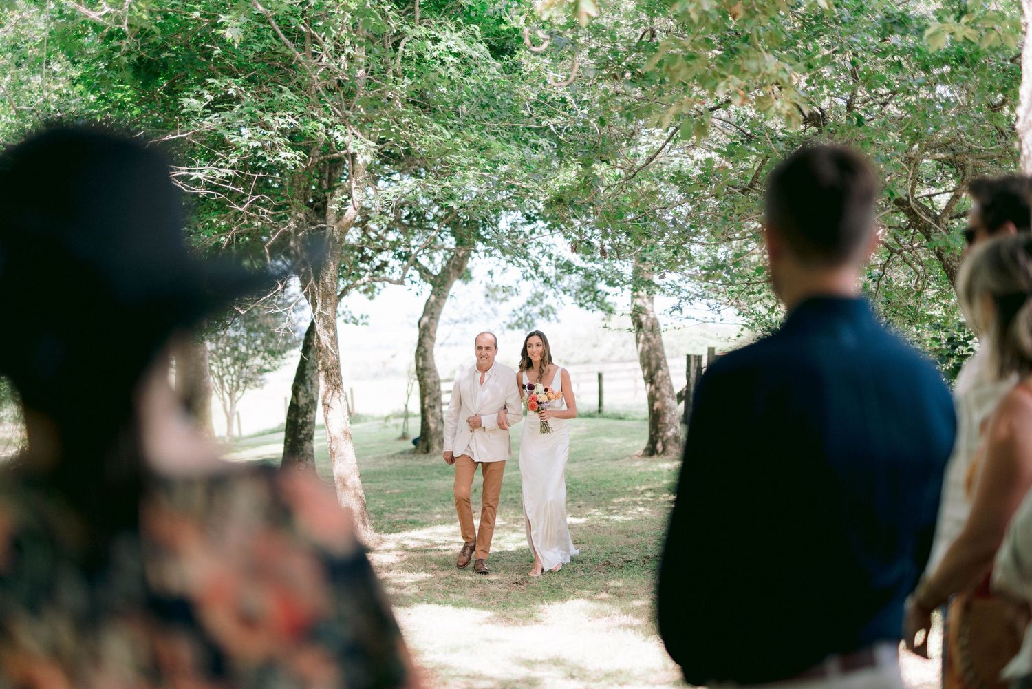 Outdoor wedding ceremony setup with guests seated under shade trees.