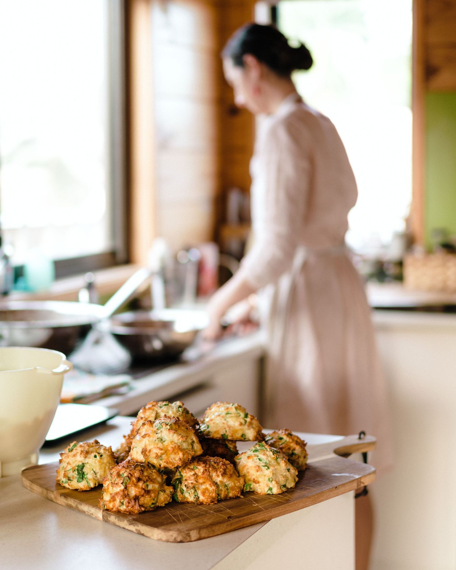 Fresh-baked golden brown biscuits cooling on a wooden cutting board in a rustic kitchen.