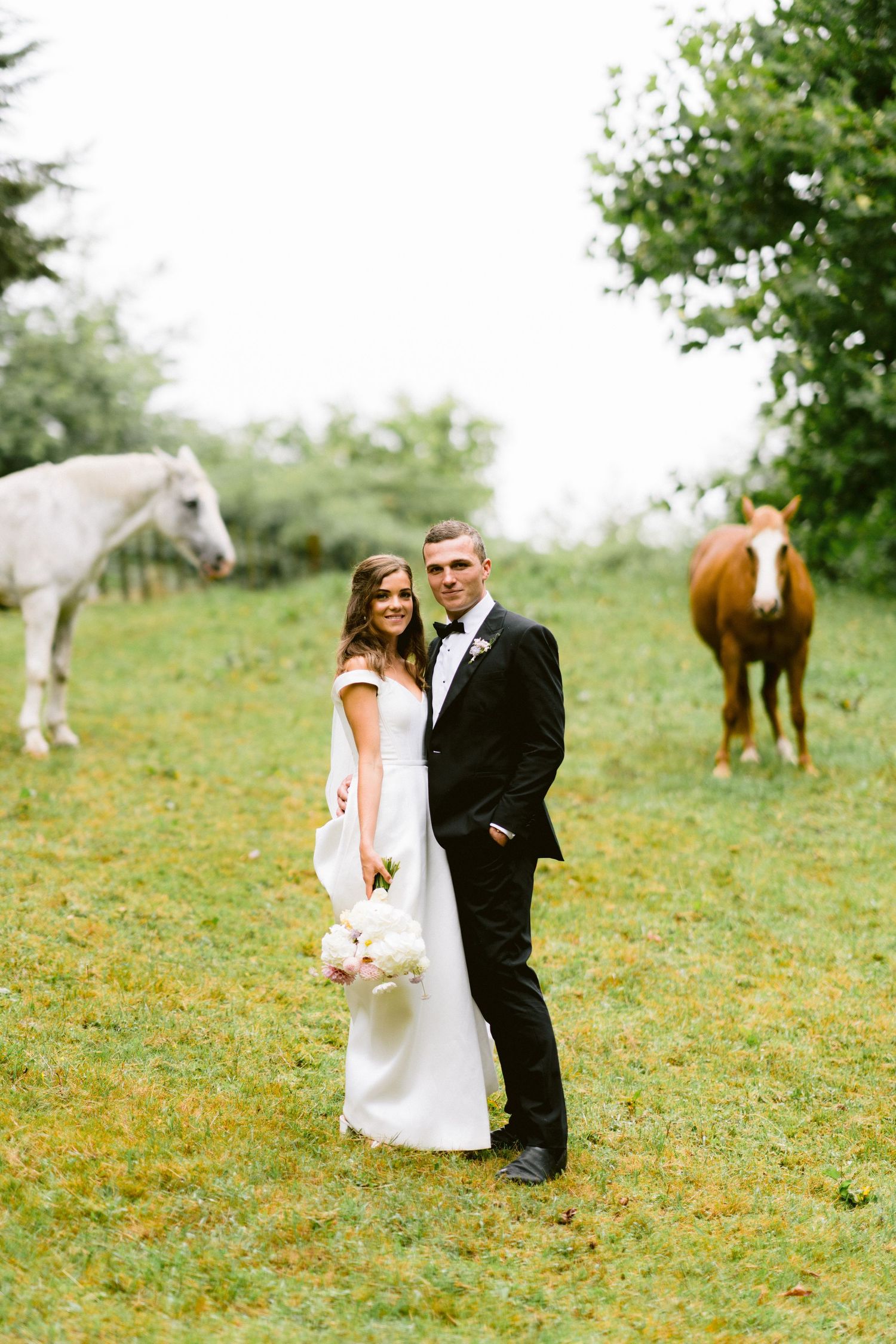 Romantic wedding portraits in a field with horses grazing in the background.