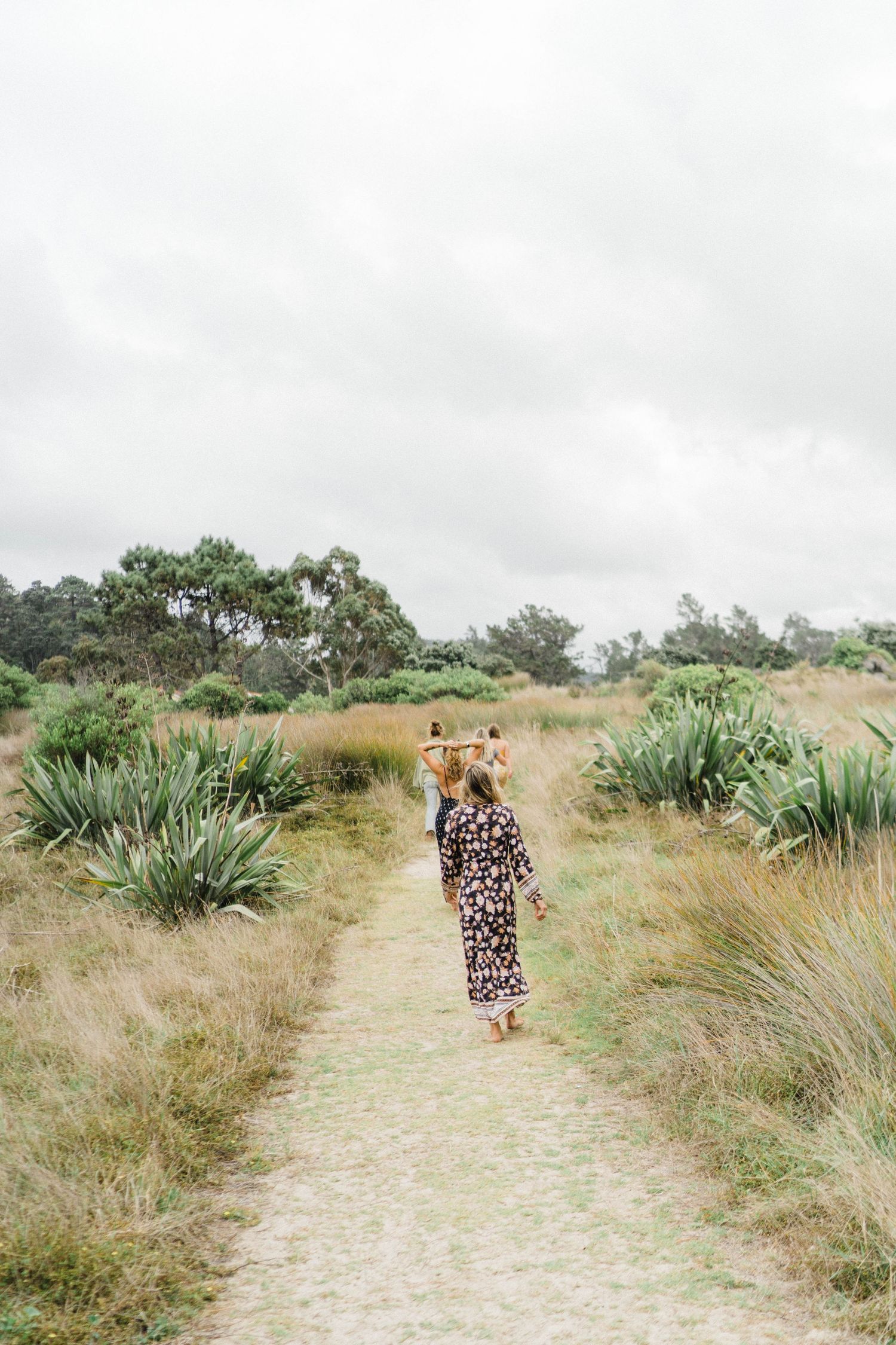 Person in leopard print dress walking along nature trail through coastal vegetation.