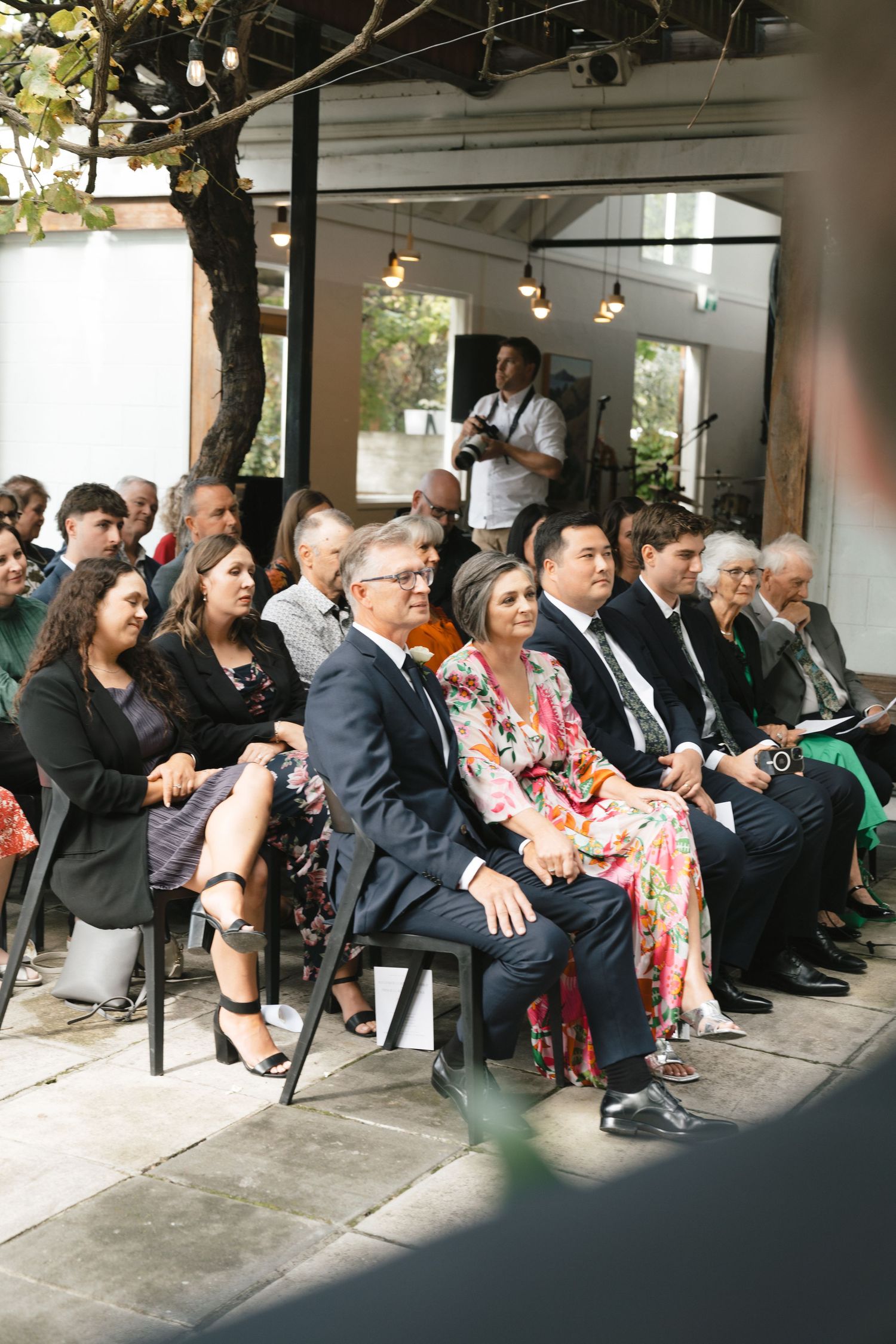 Guests seated in rows at an elegant outdoor ceremony with string lights overhead.