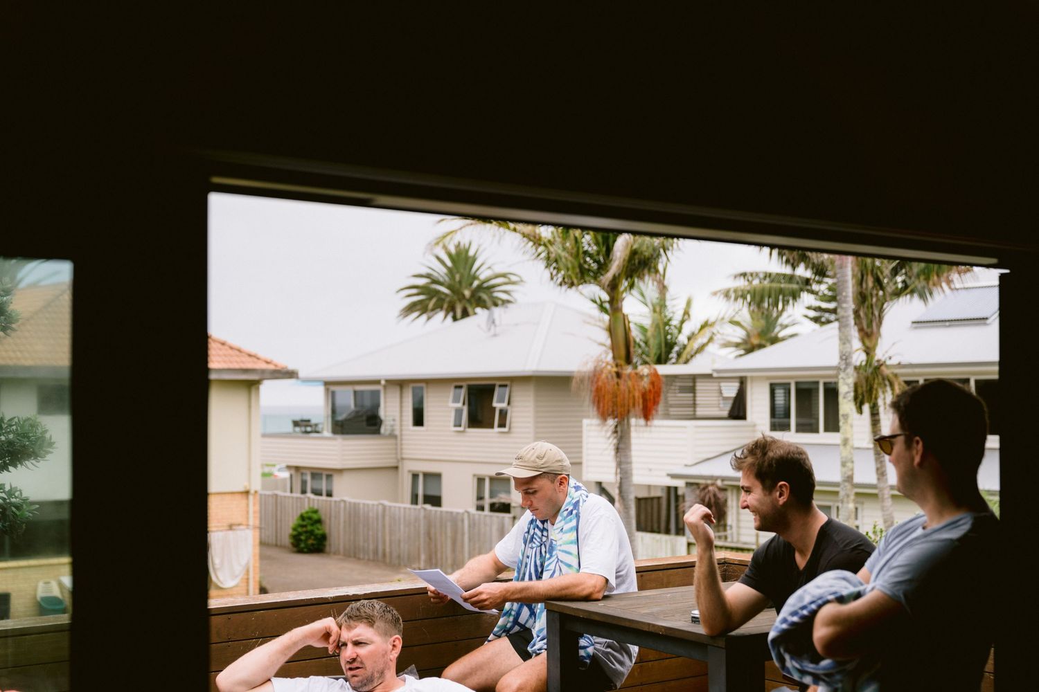 People gathered on a balcony overlooking residential buildings with palm trees visible in the background.
