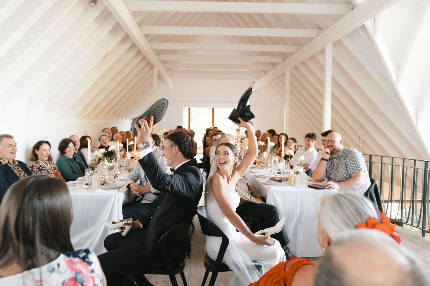 Wedding reception celebration in bright white venue with vaulted ceiling and festive atmosphere.