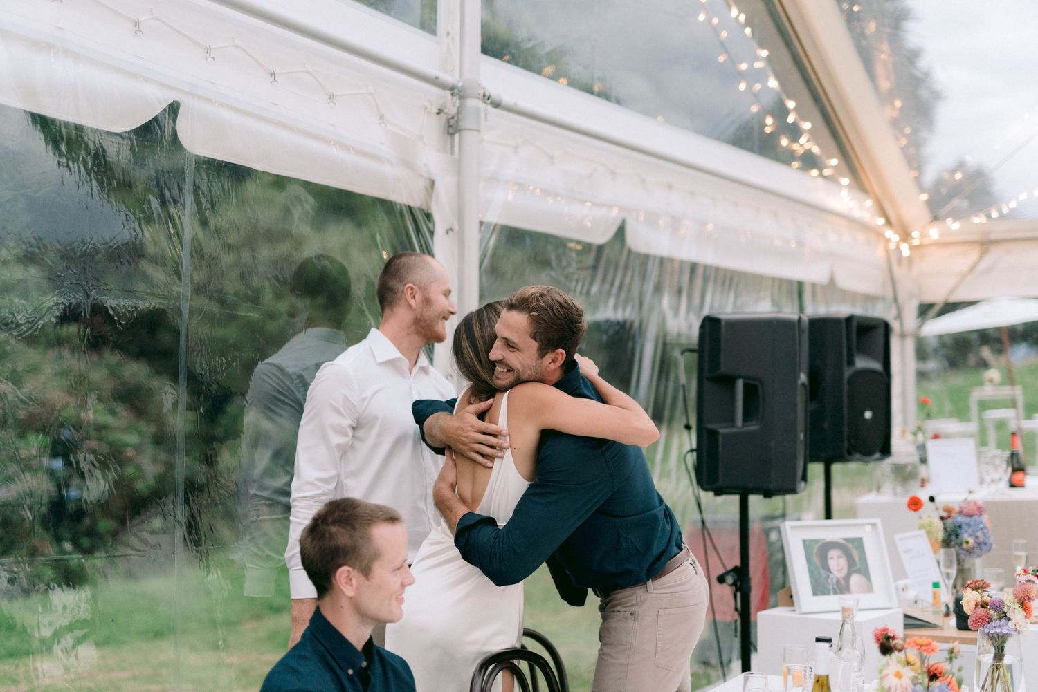 Guests celebrate under a white wedding tent during an emotional reception moment.