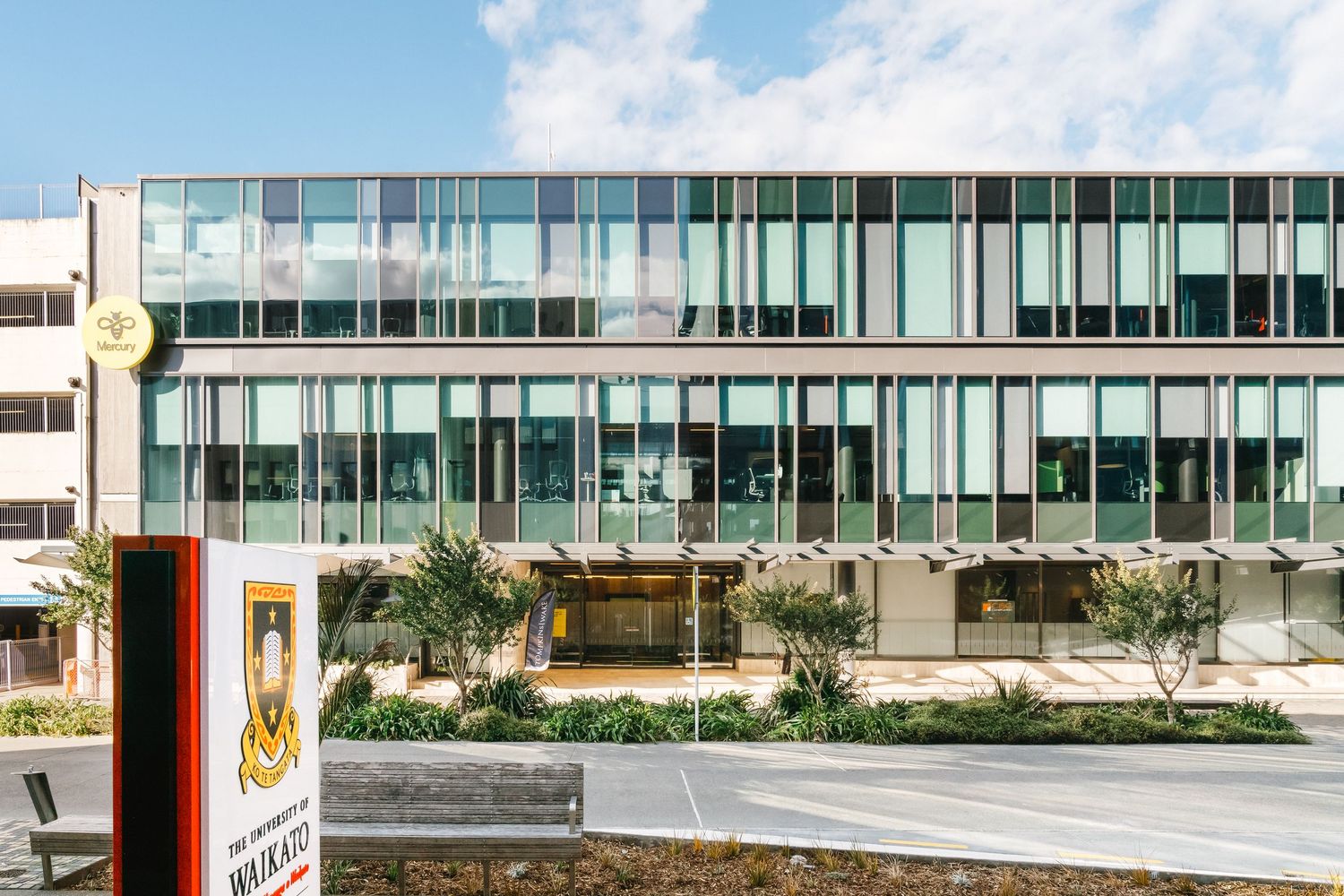 Modern office building exterior with glass facade and landscaping along a commercial street entrance.