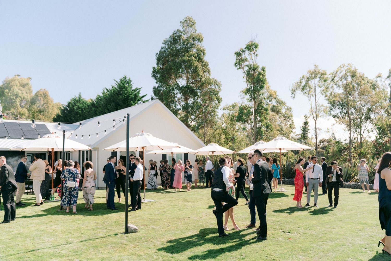 Outdoor wedding reception with guests mingling under string lights and white tent.