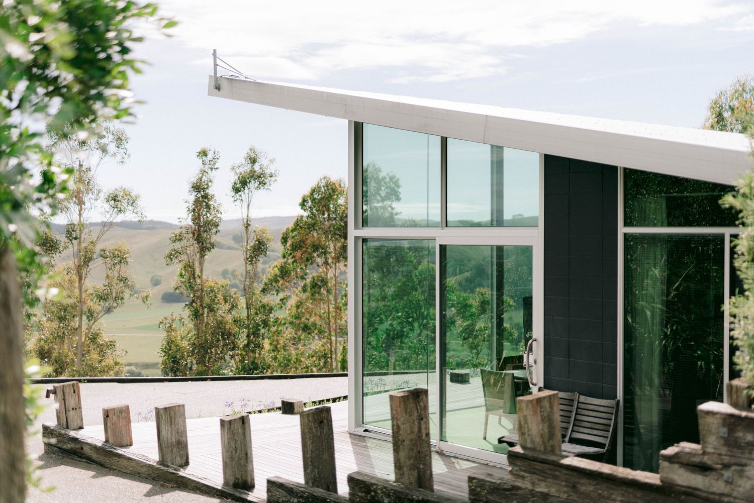 Modern glass house with outdoor seating overlooking a scenic mountain landscape.